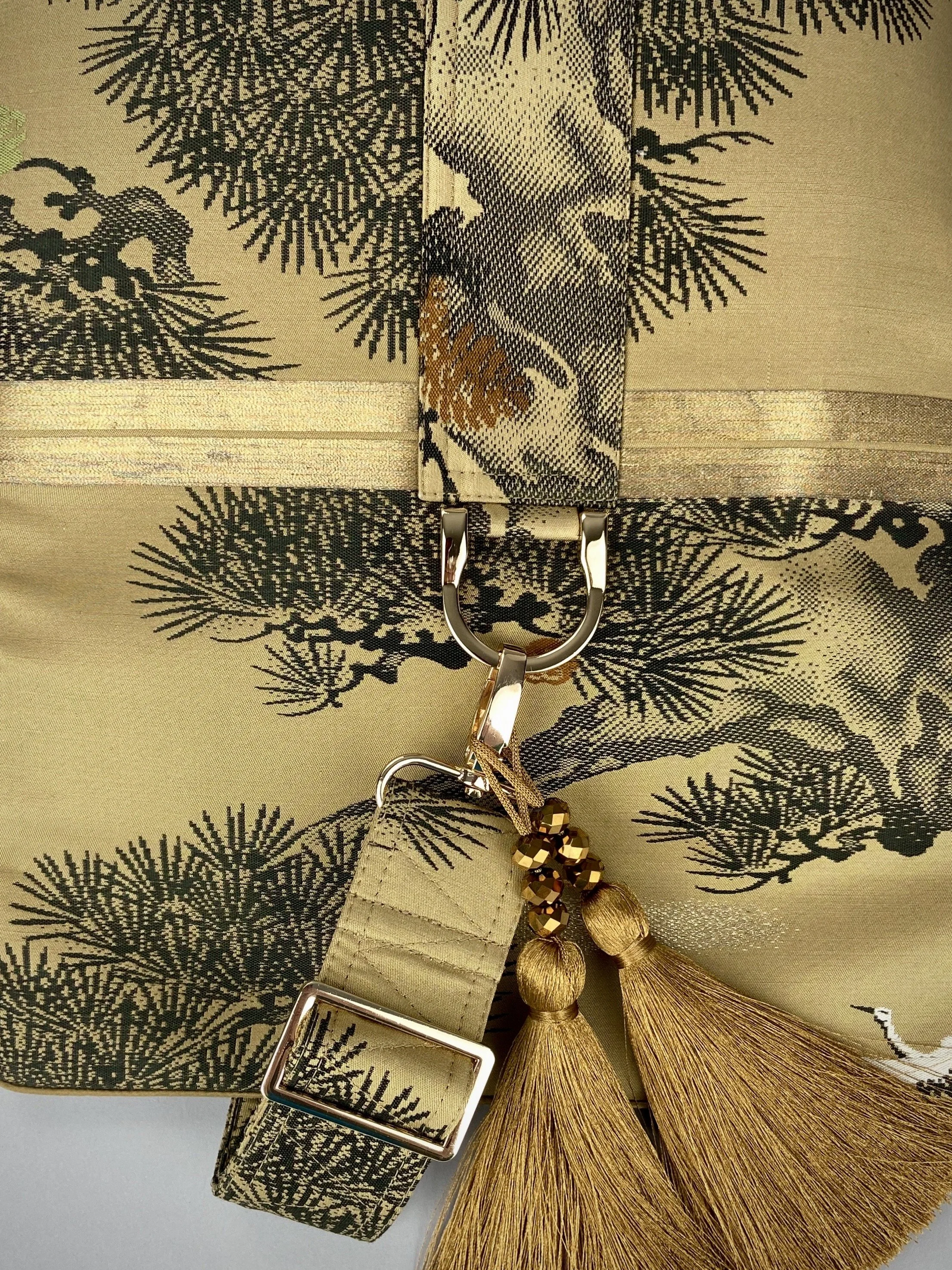 Closeup of olive green Matsu pine vintage obi silk shoulder bag with crane design, gold thread detailing and matching fabric tassel charm by Kirsty Chivers