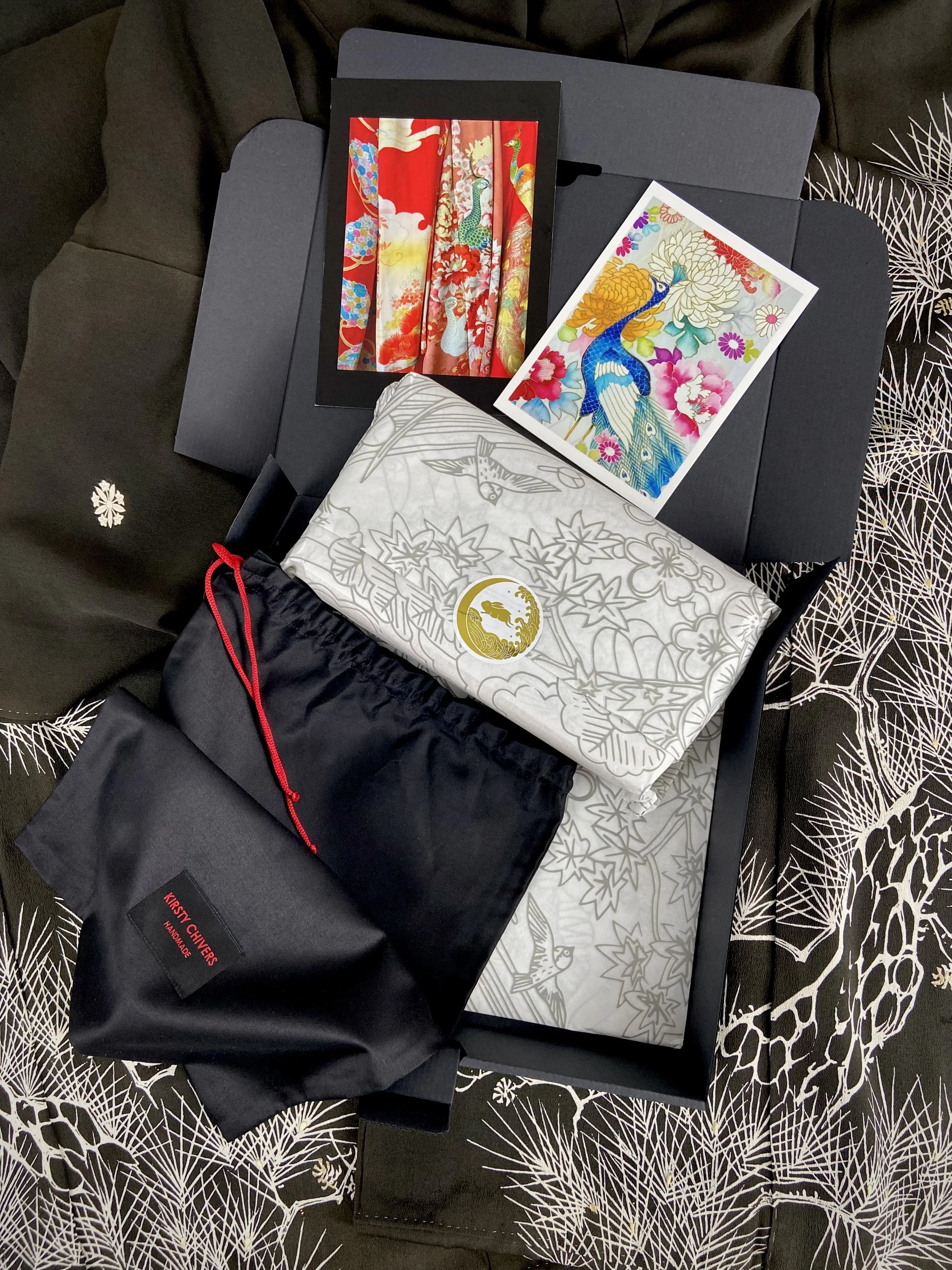 Kirsty Chivers Handmade bespoke packaging, tissue paper with hand drawn design, black cotton dust bag and postcards, presented on a black silk kimono background