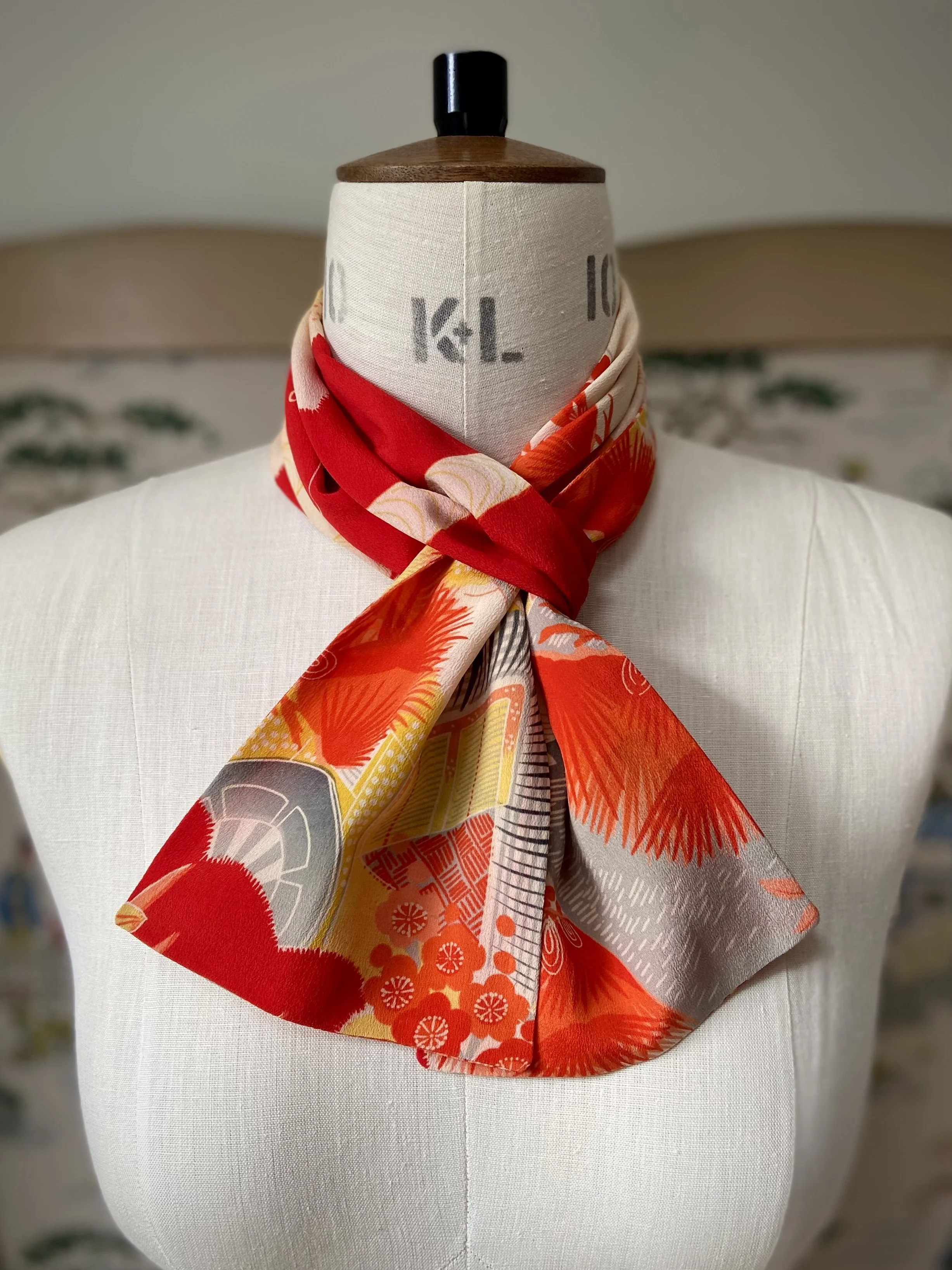 Closeup of bright vermillion red and yellow scarf presented on a dress stand, with printed blossom design, handmade from repurposed Japanese kimono crepe silk by Kirsty Chivers