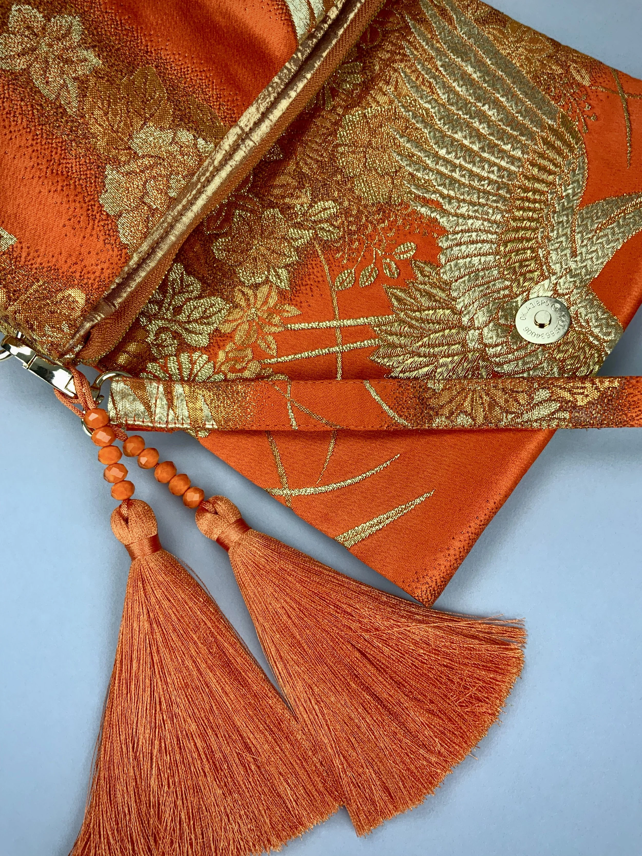 Closeup of vibrant orange evening bag with gold copper crane and blossom design, handmade from vintage obi silk by Kirsty Chivers