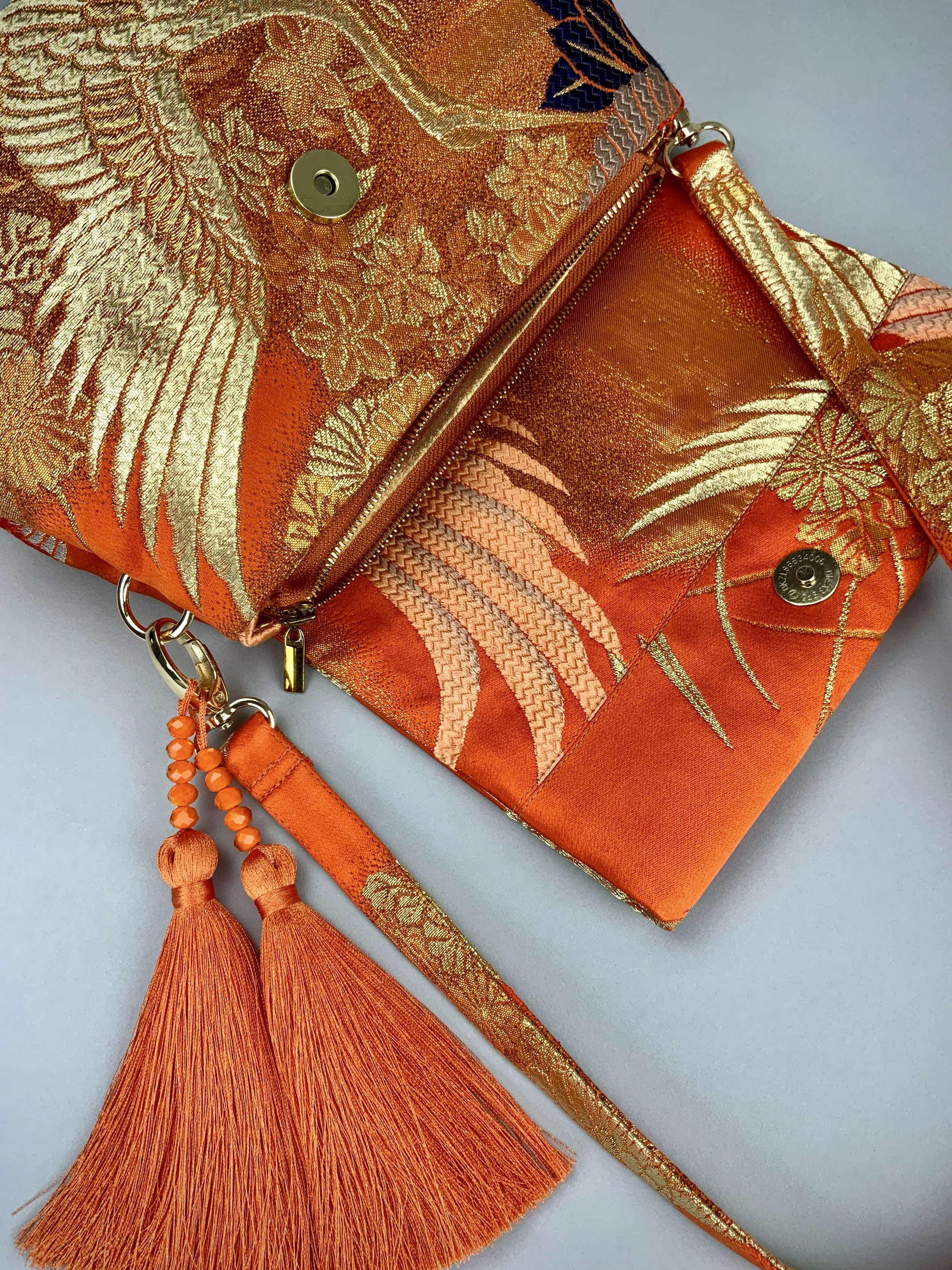 Closeup of vibrant orange evening bag with gold copper crane and blossom design, handmade from vintage obi silk by Kirsty Chivers
