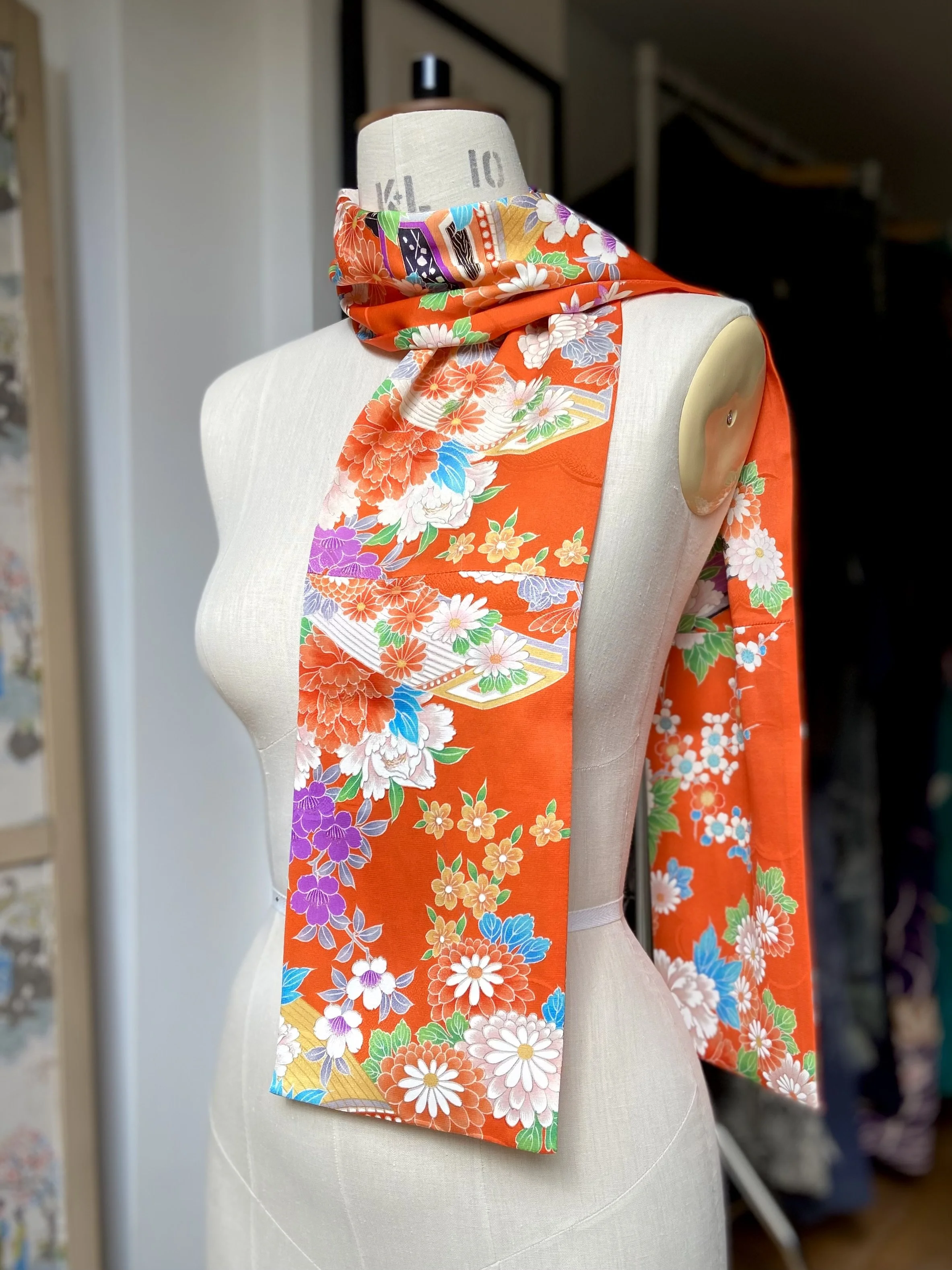 Orange scarf presented on a dress stand. It has a blossom print and is made from rinzu kimono silk by Kirsty Chivers