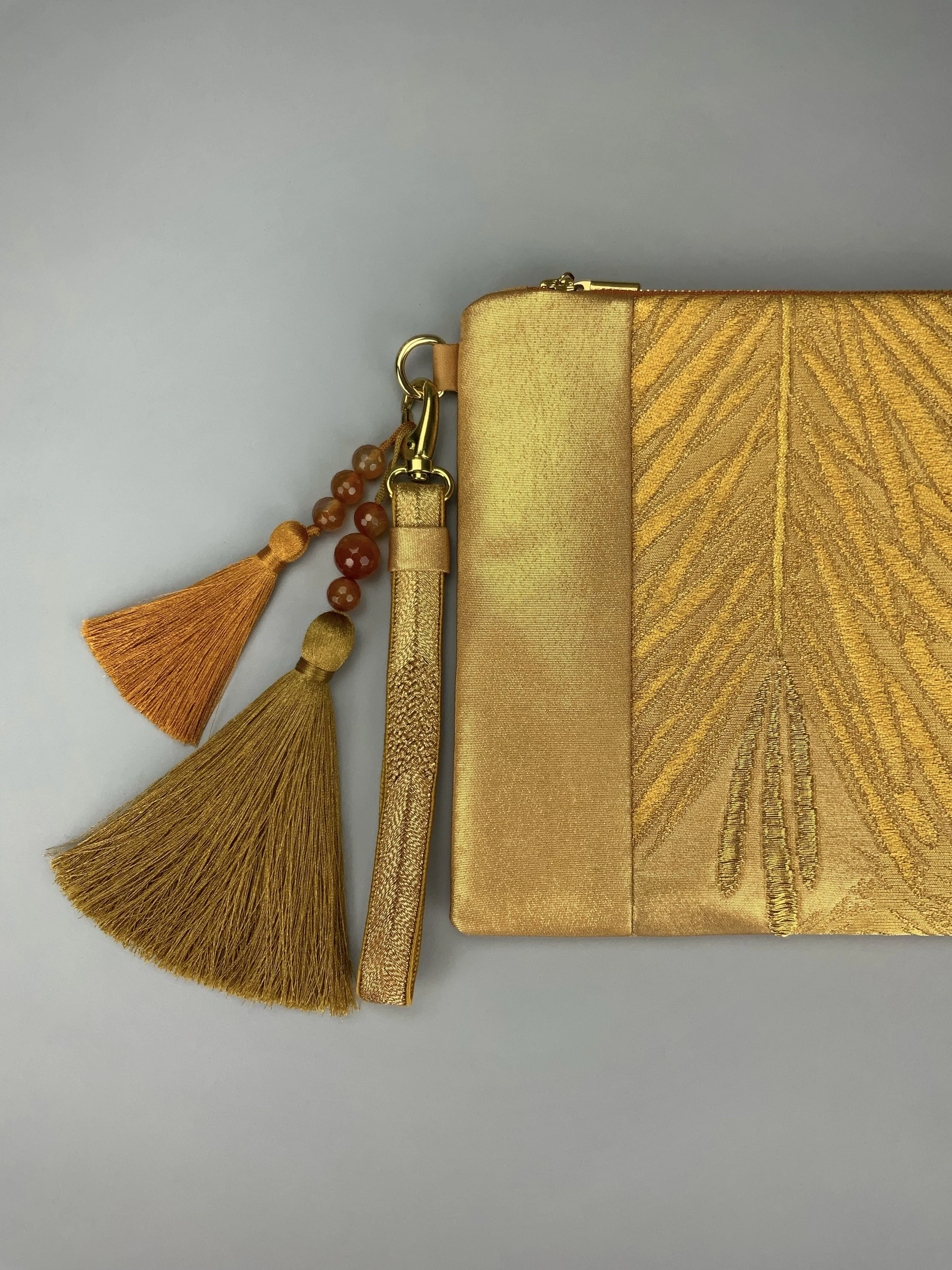 Closeup of glittery gold clutch with leaf design and silk tassel charms, handmade by Kirsty Chivers