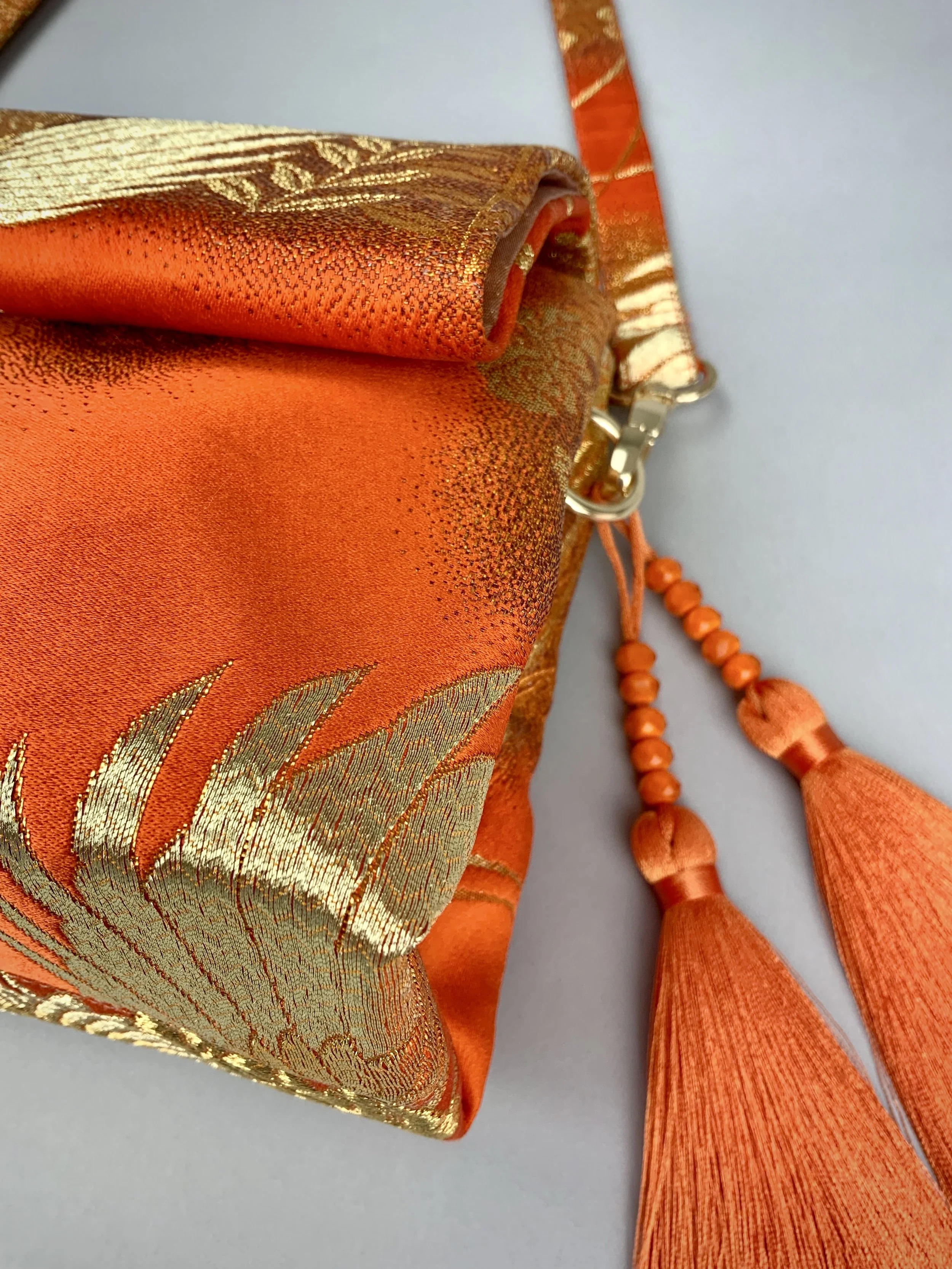 Closeup of vibrant orange evening bag with gold copper crane and blossom design, handmade from vintage obi silk by Kirsty Chivers