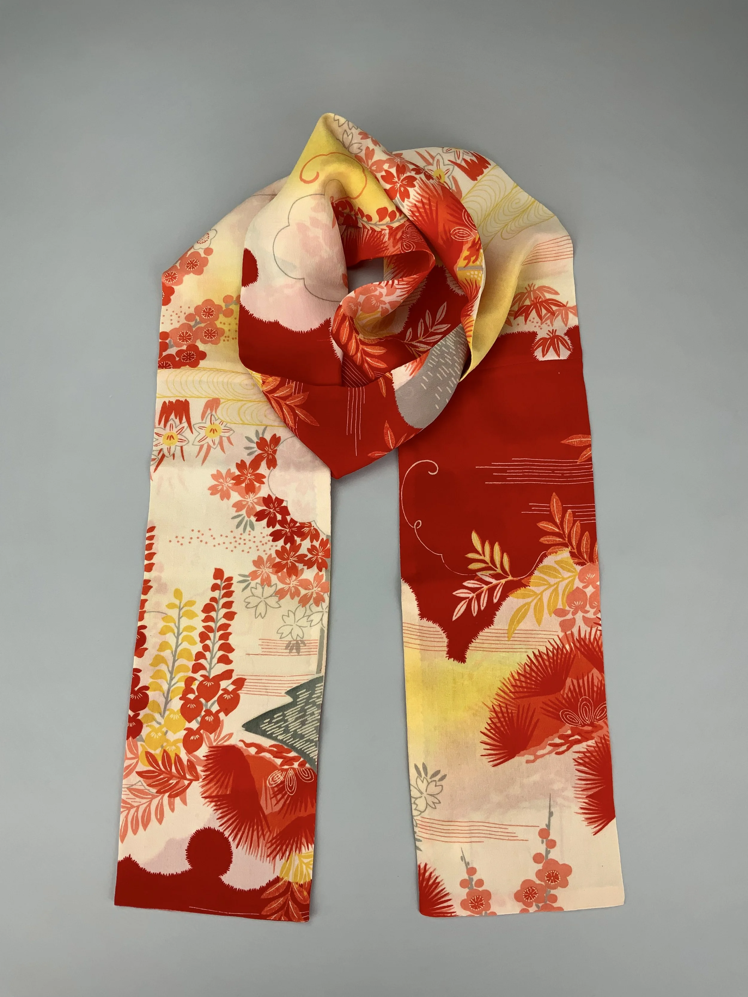Flatlay of vibrant red and yellow scarf with printed blossom design, handmade from repurposed Japanese kimono crepe silk by Kirsty Chivers