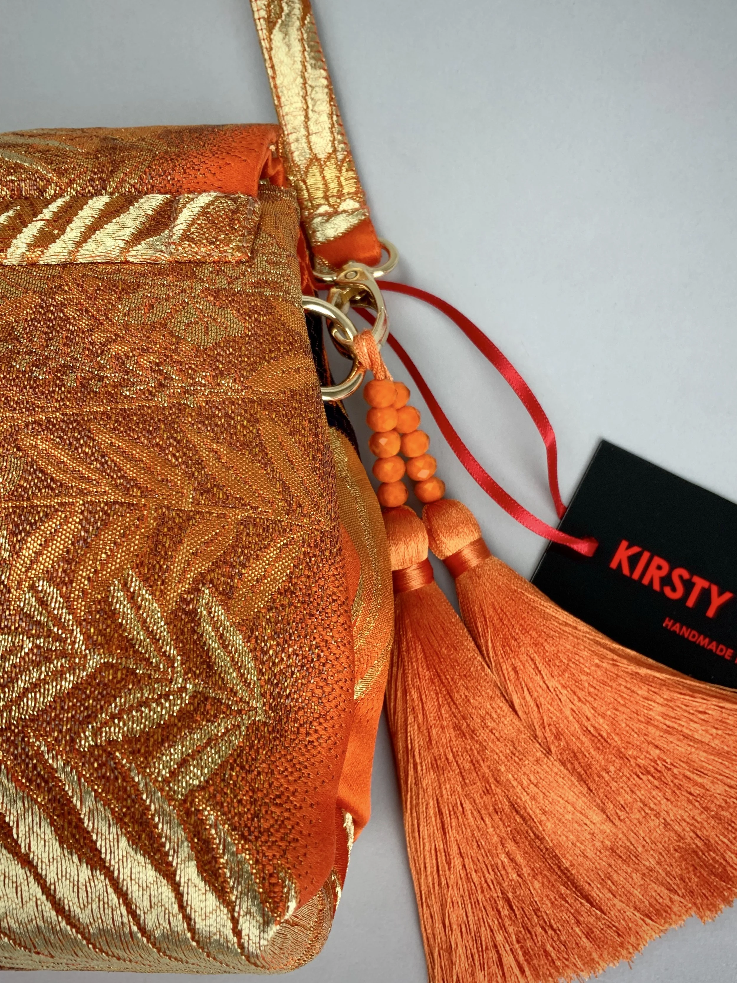 Closeup of vibrant orange evening bag with gold copper crane and blossom design, handmade from vintage obi silk by Kirsty Chivers