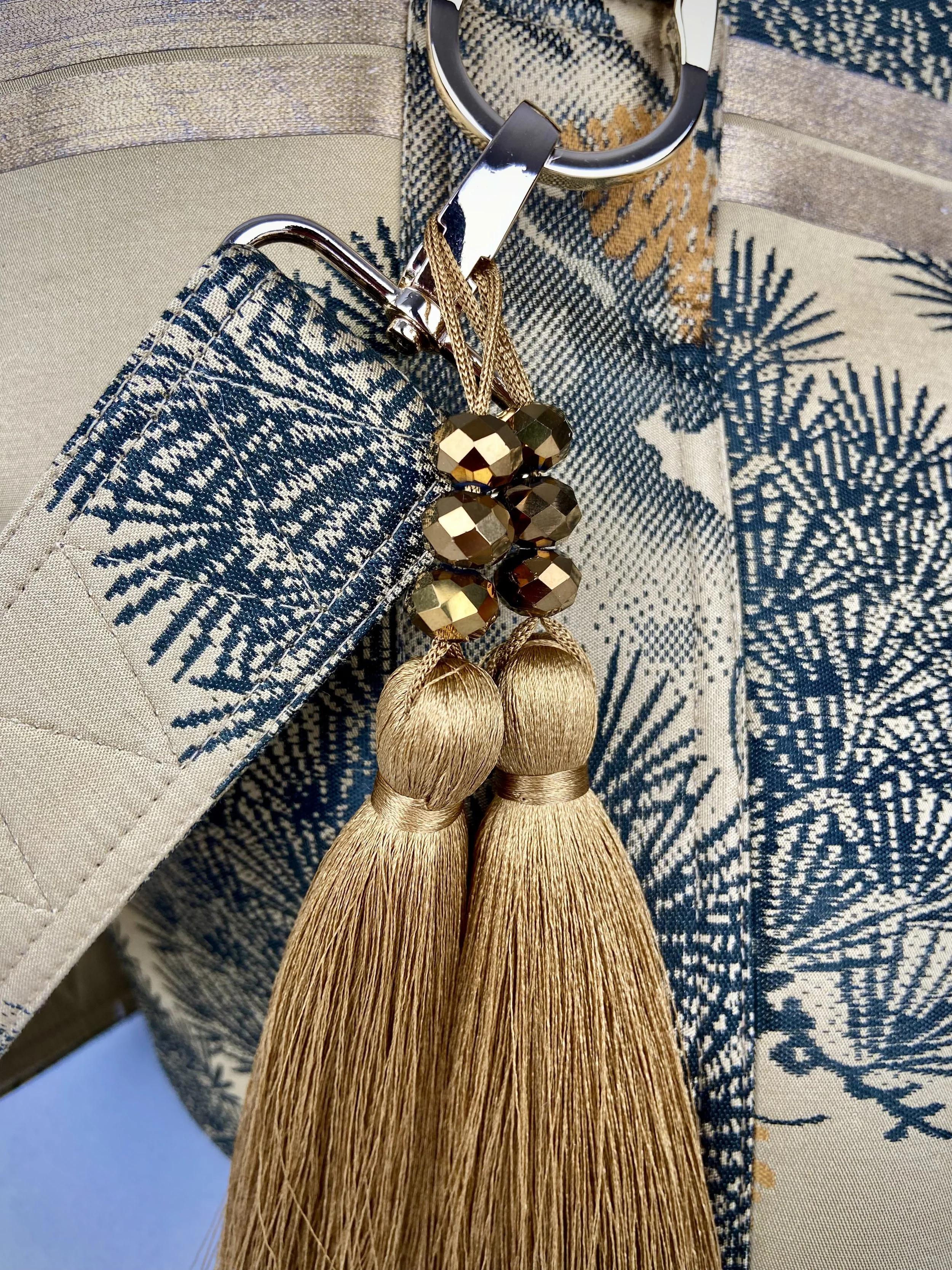 Closeup of olive green Matsu pine vintage obi silk shoulder bag with crane design, gold thread detailing and matching fabric tassel charm by Kirsty Chivers