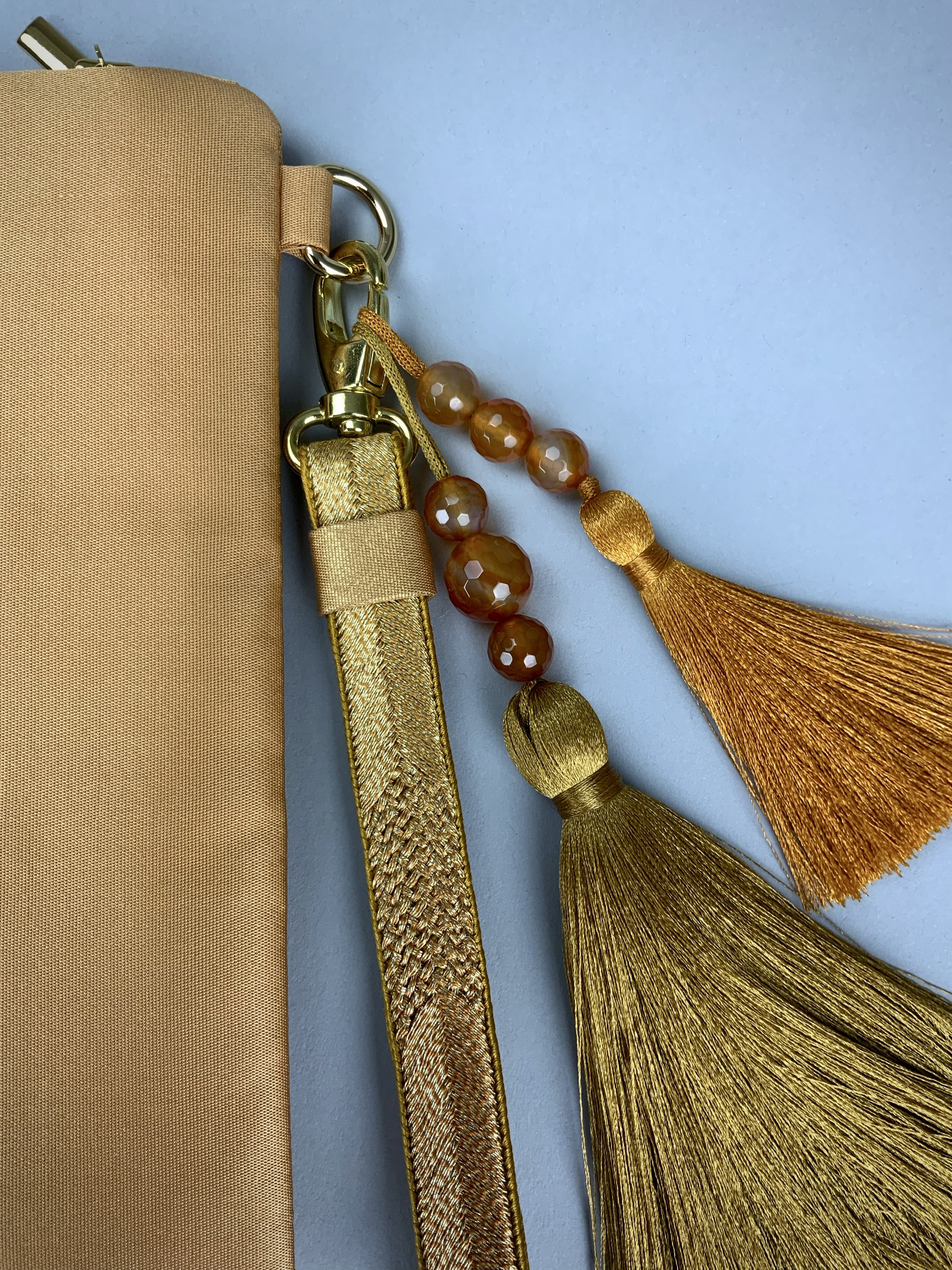 Closeup of glittery gold clutch with leaf design and silk tassel charms, handmade by Kirsty Chivers