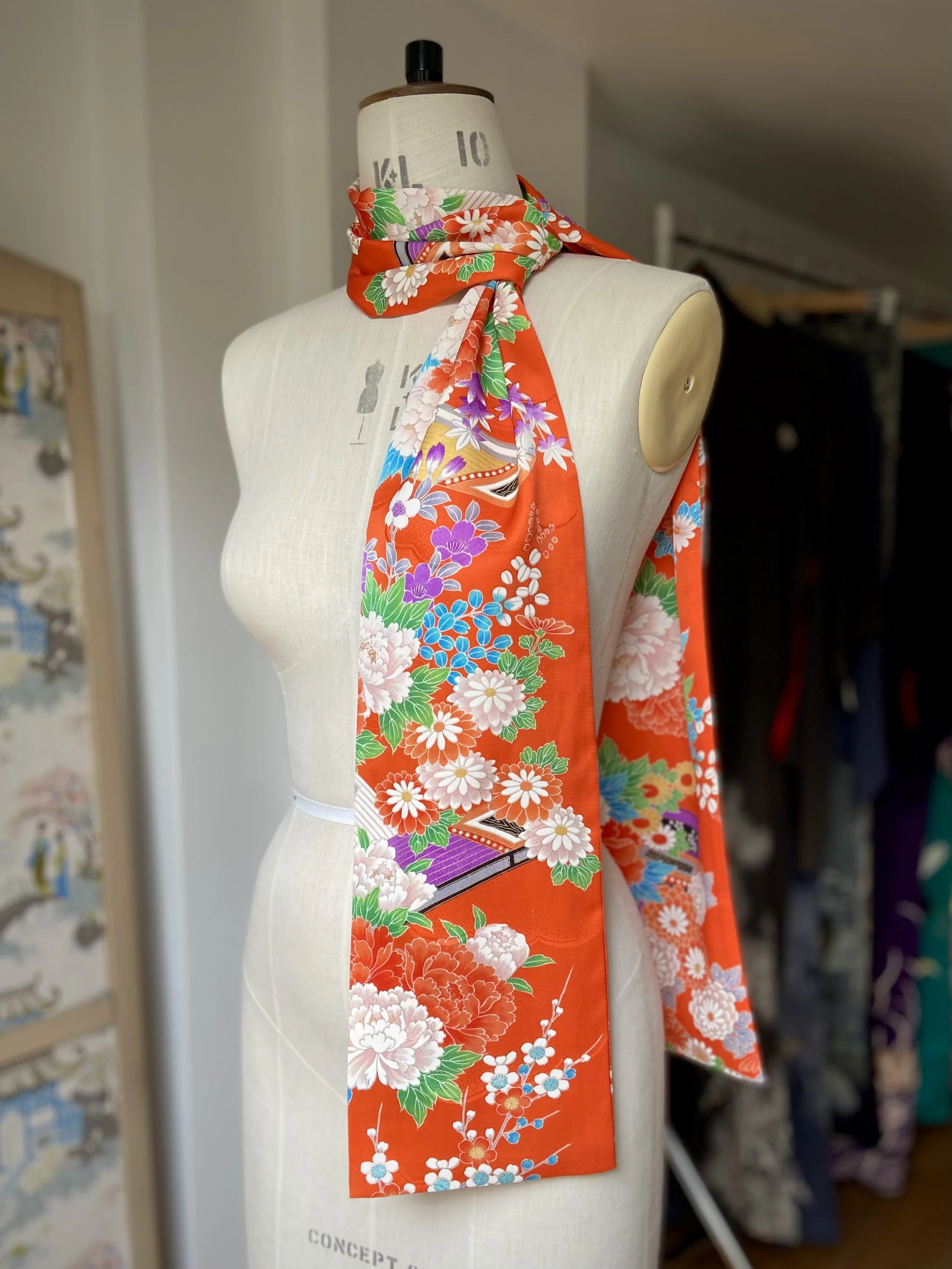 Orange scarf presented on a dress stand. It has a blossom print and is made from rinzu kimono silk by Kirsty Chivers