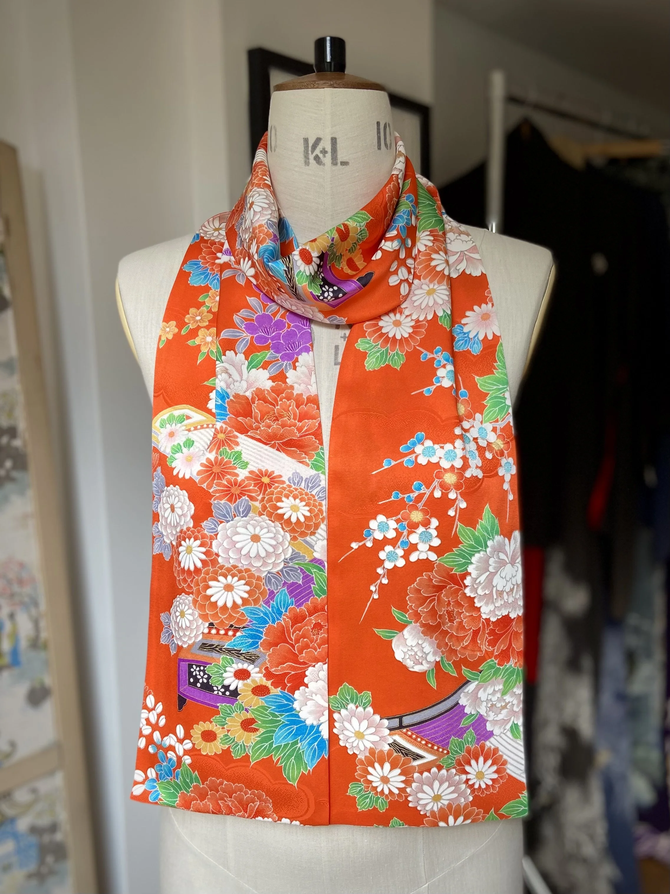 Orange scarf presented on a dress stand. It has a blossom print and is made from rinzu kimono silk by Kirsty Chivers