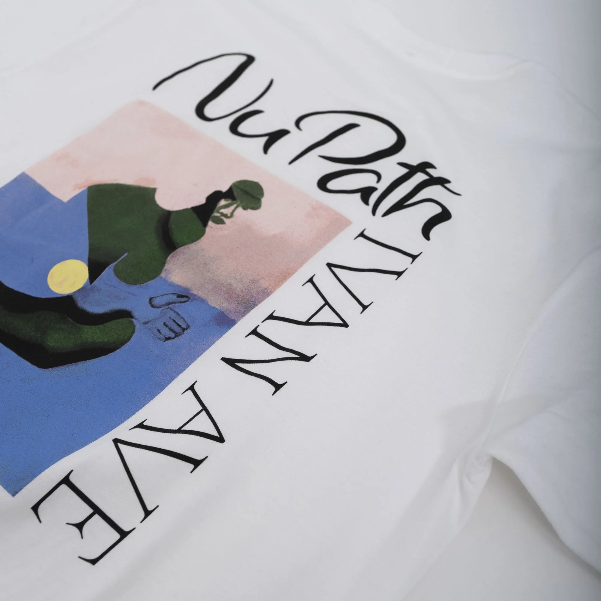 A white fabric with black cursive text that reads 'NU PATH Ivan Ave' and a colorful illustration of a person in green shirt and blue hat, against a pink and blue background.