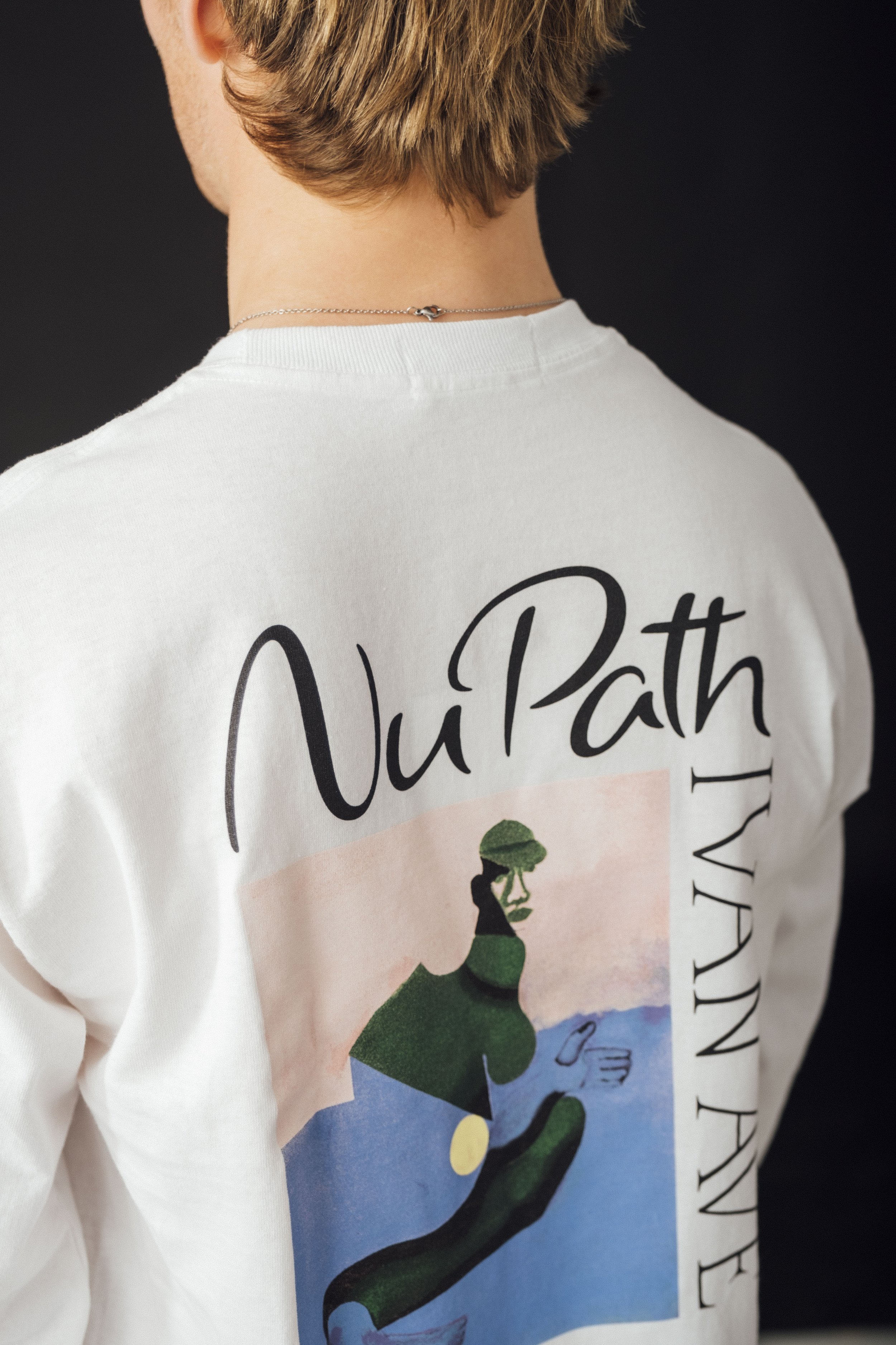 Back of a person wearing a white t-shirt with a colorful graphic and text, with a black background.