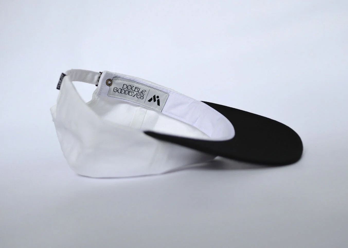 A black and white baseball cap flipped inside out, displaying the interior tag that reads "DOUBLE GOODBYES" and features a small logo.