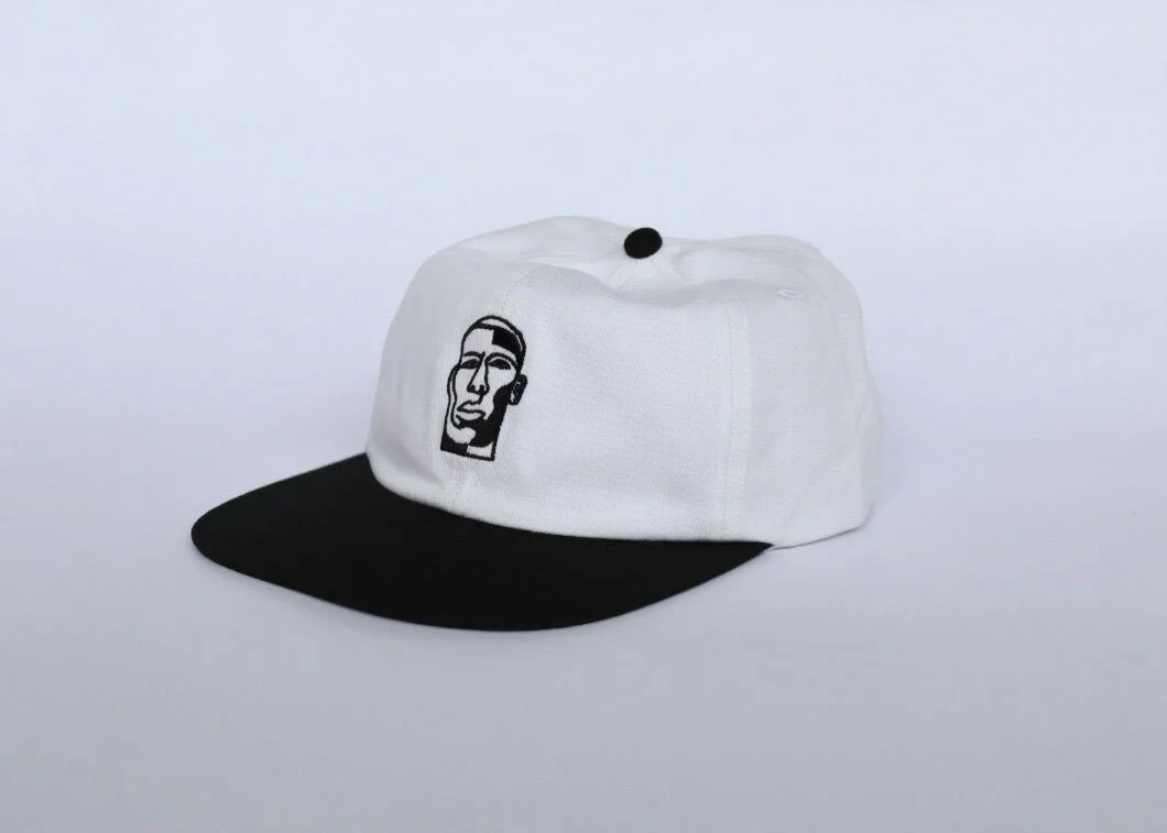 A white and black baseball cap with a logo of a stylized face on the front.