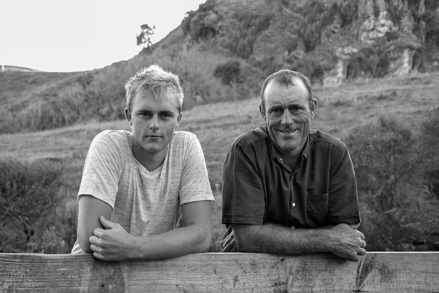 father and son on farm leaning over railing togheter 