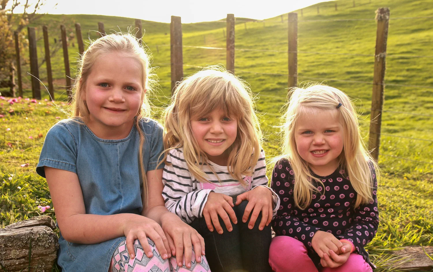three blonde sisters sitting together on farm