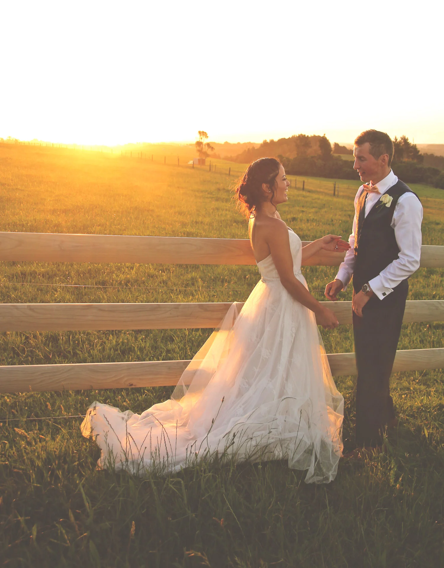 bride_and_groom_on_wedding_day_at_sunset_looking_at_eachother_in_love_by_fence_lovely_yellow_colours_on_farm.jpg