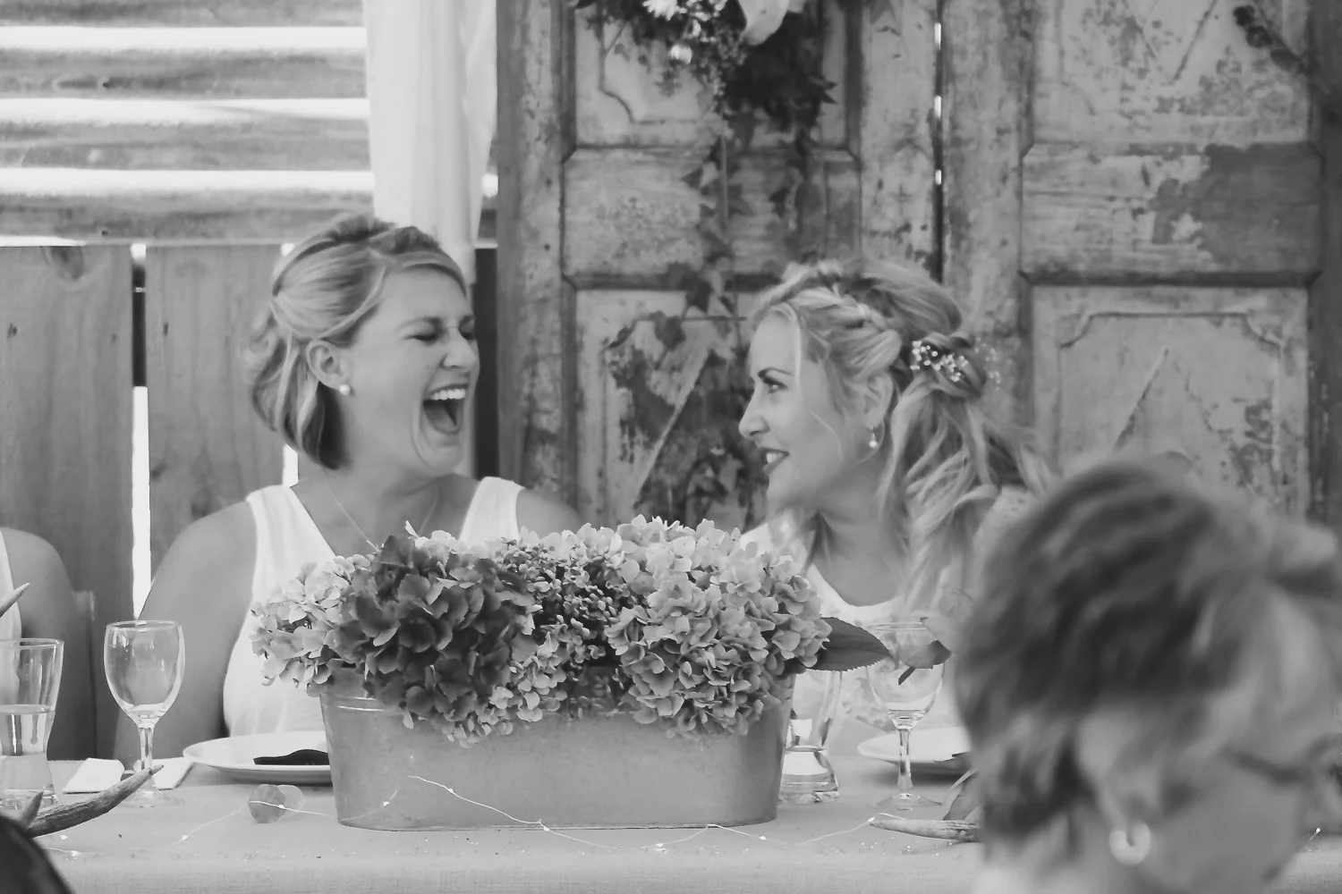 bride_and_maid_of_honour_laughing_together_at_wedding_reception_Lovely_flowers_in_front_of_them_rustic_vintage_wedding_theme.jpg