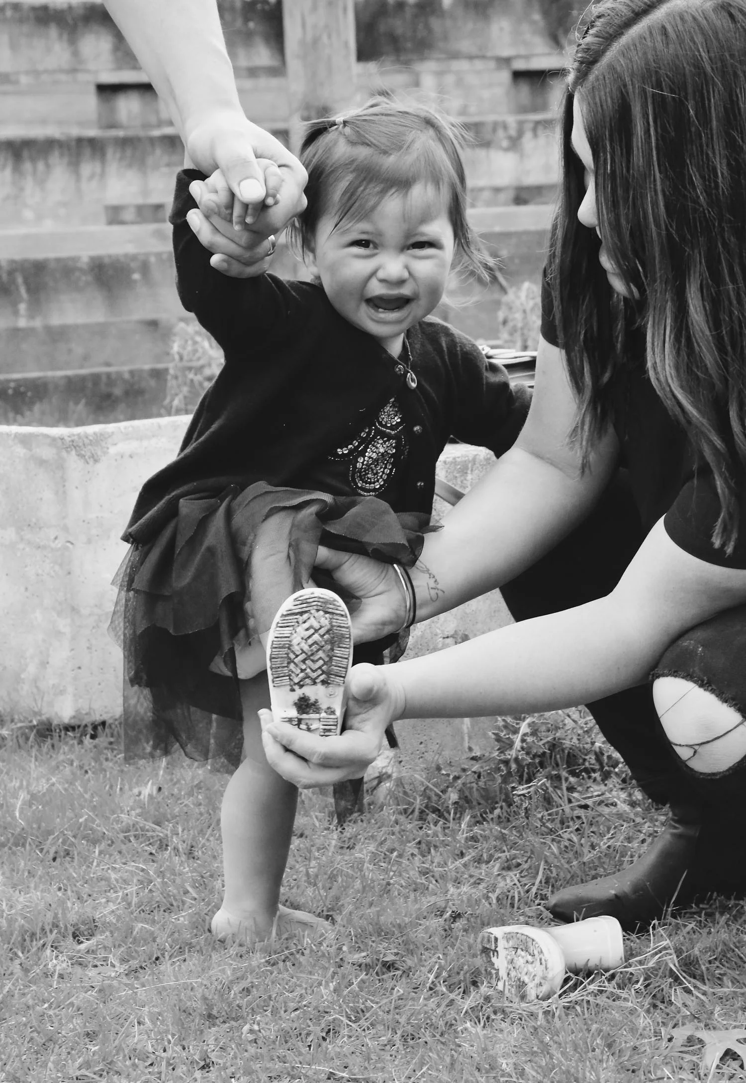 baby_girl_crying_putting_on_boots_mum_helping_her_black_and_white_image.jpg