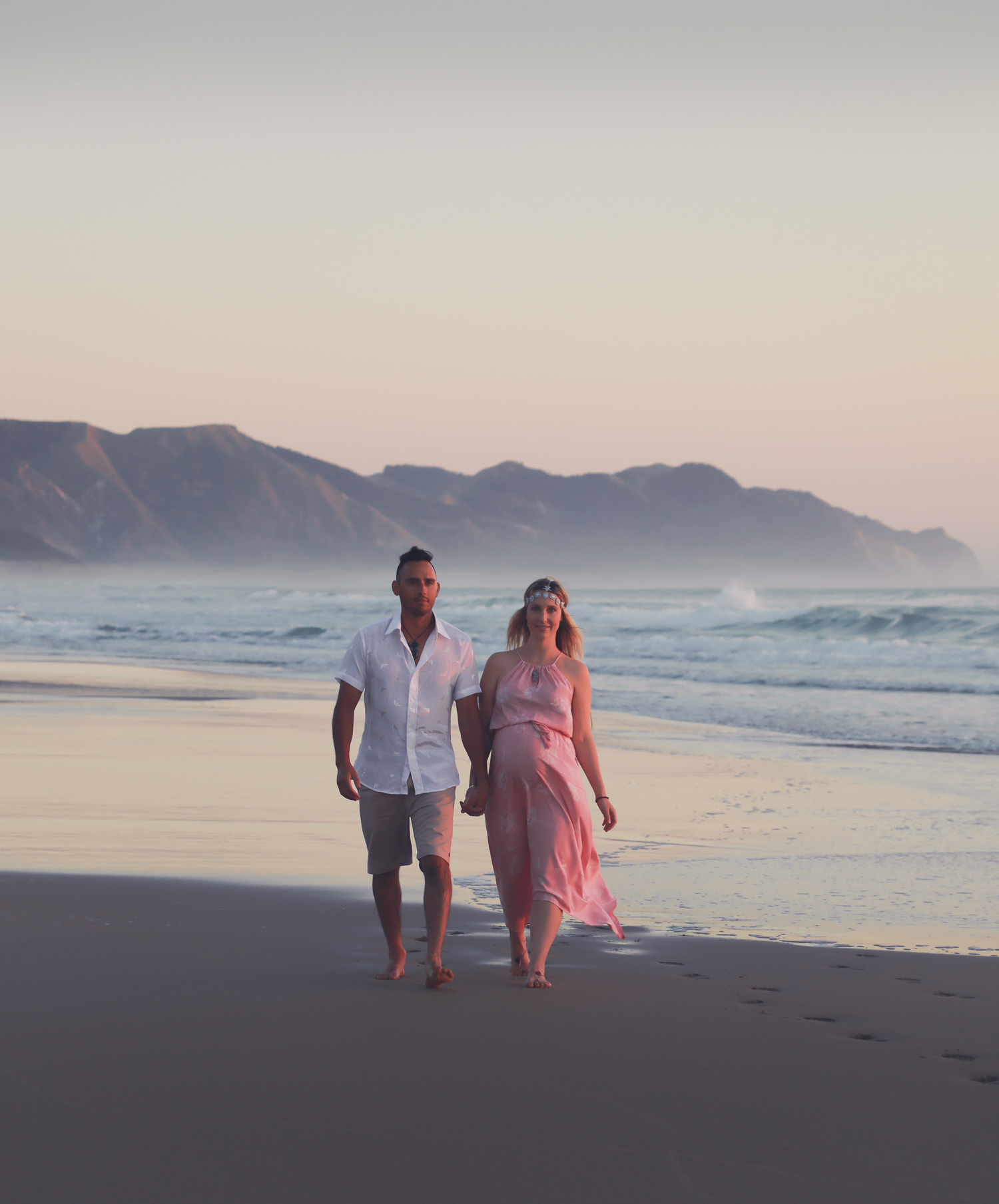 pregnant woman at beach at sunrise with husband walking along beach