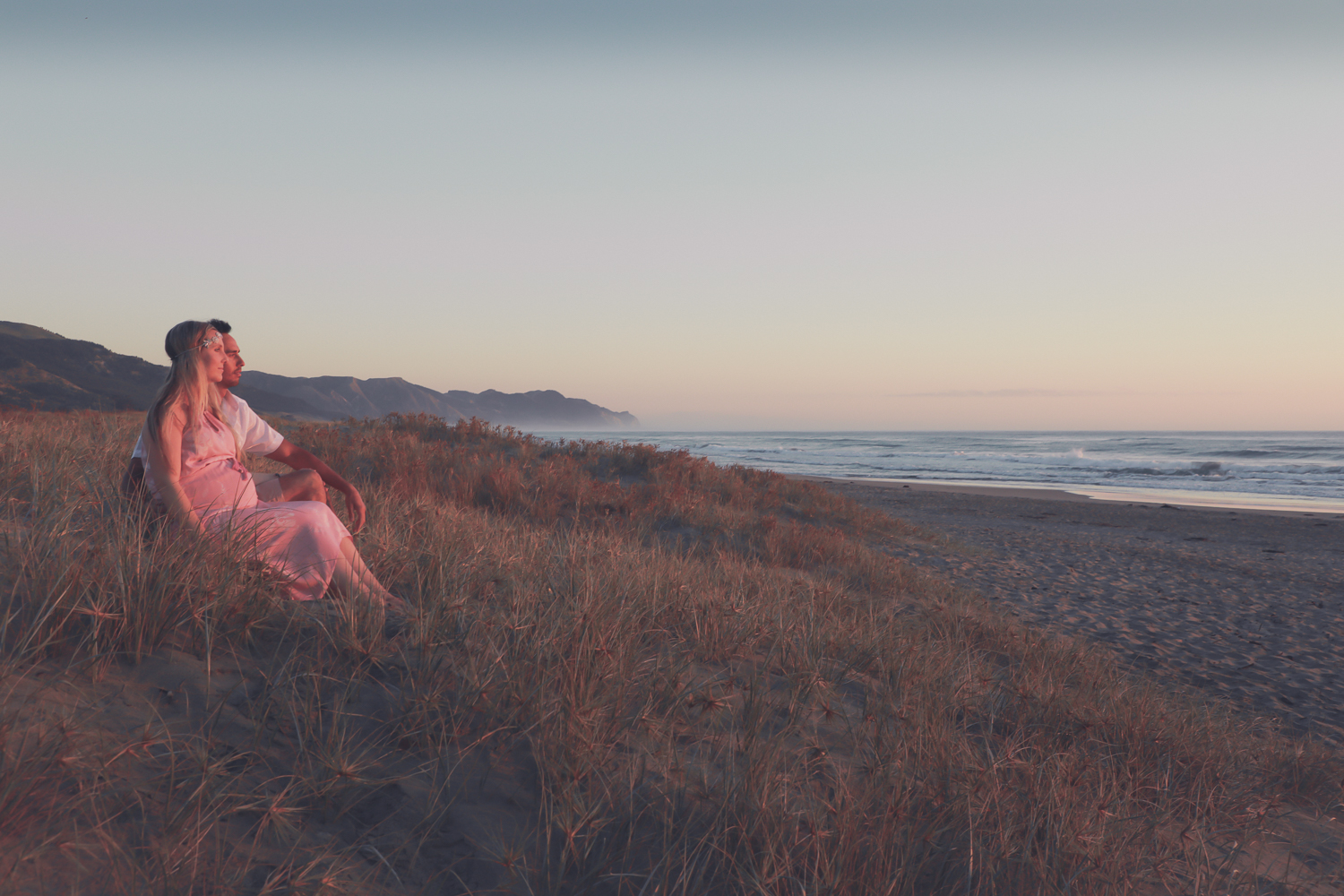pregnant woman at beach at sunrise with husband looking out to ocean