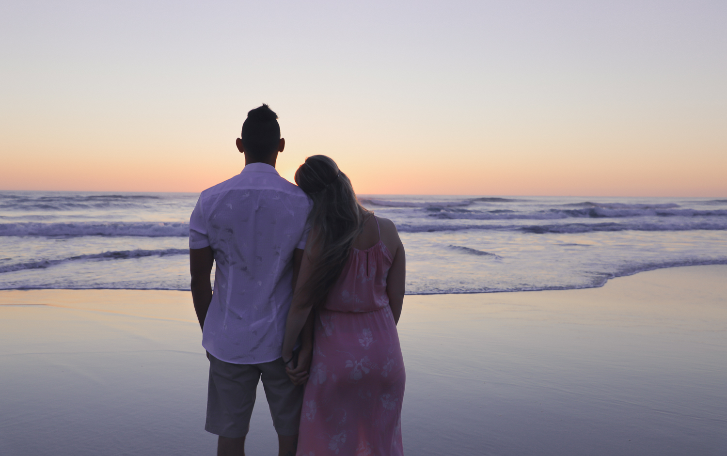 pregnant woman at beach at sunrise with husband looking out to ocean