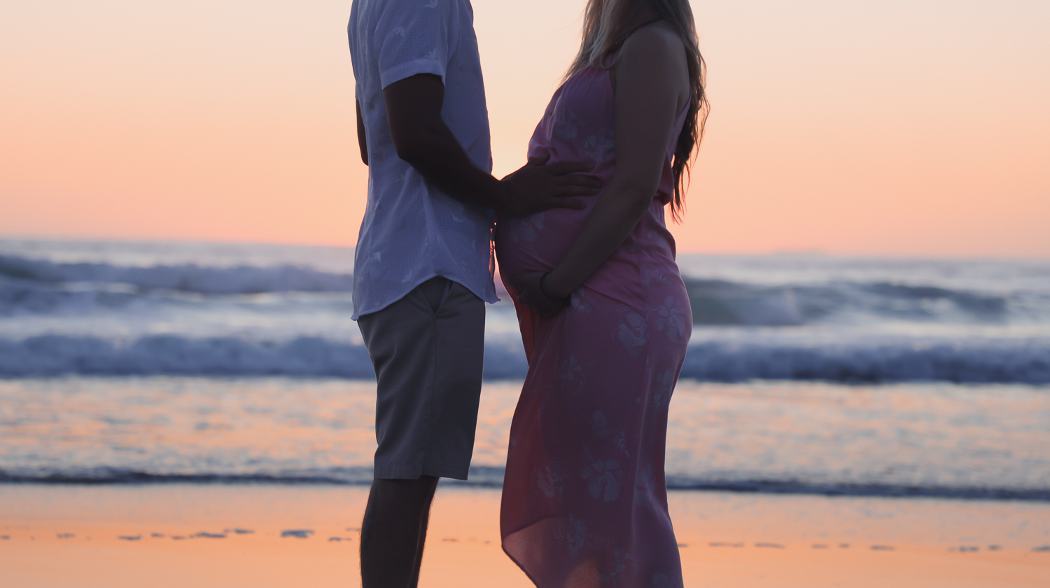pregnant woman at beach at sunrise with husband looking out to ocean