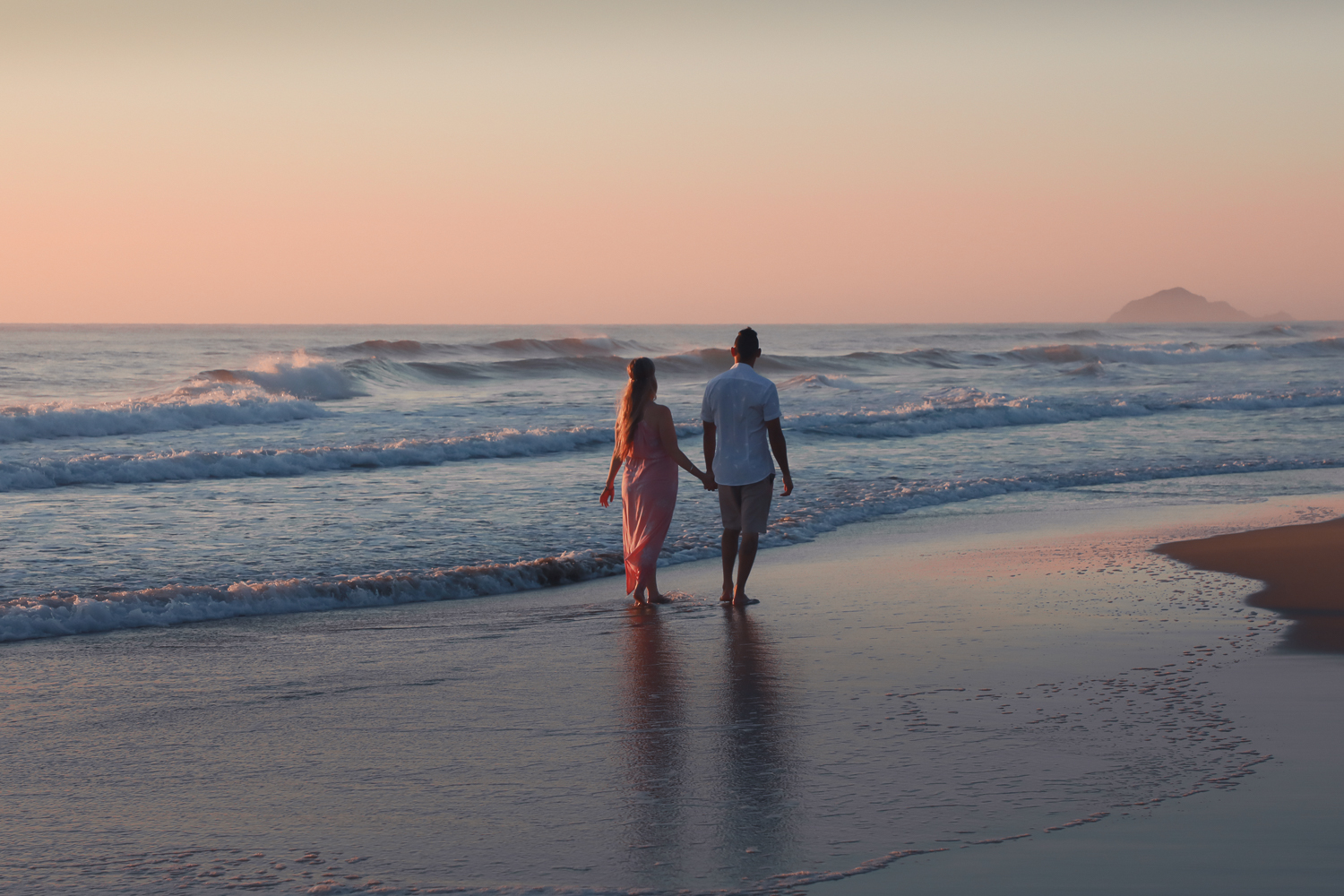 pregnant woman at beach at sunrise with husband looking out to ocean
