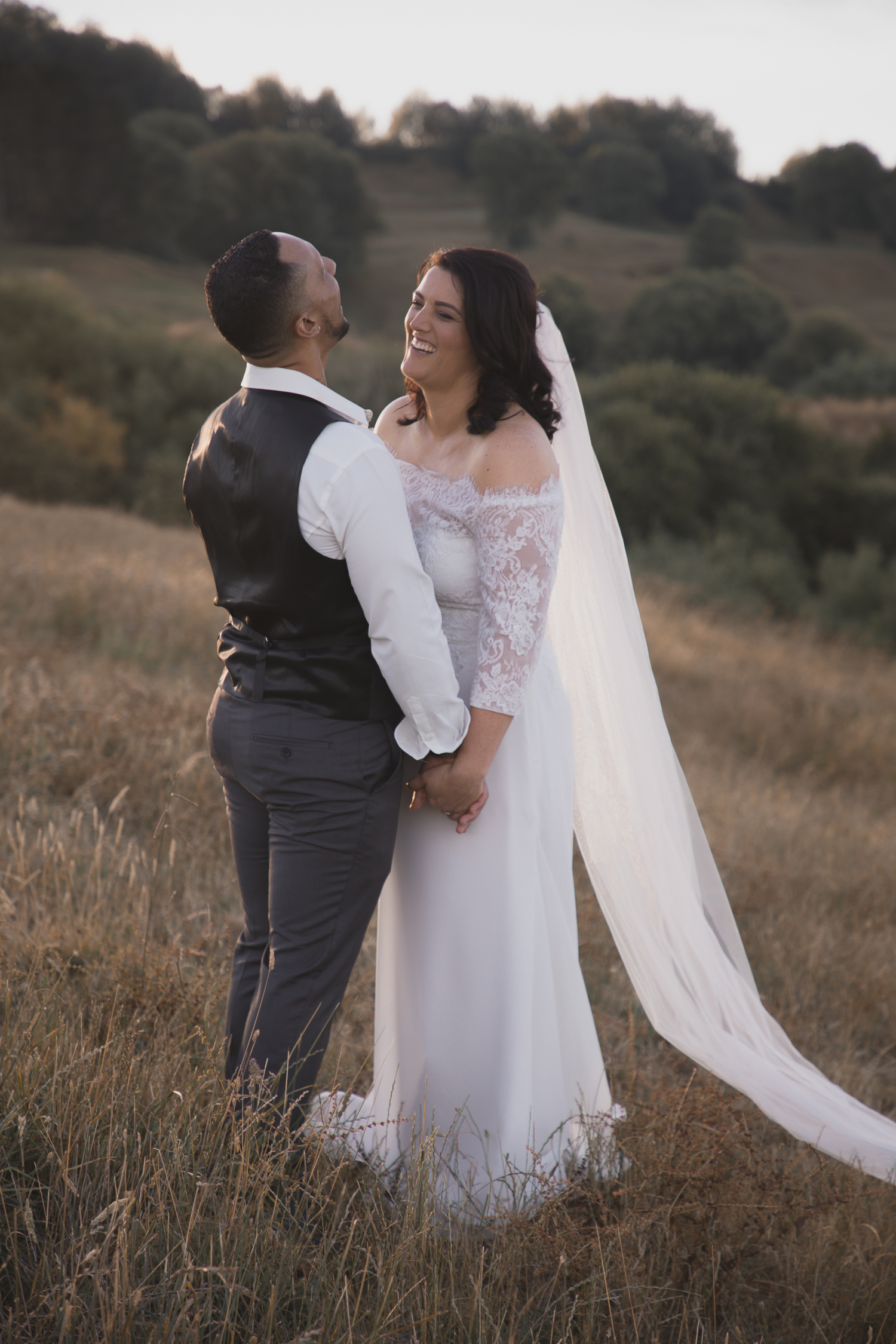 bride and groom laughing together on farm at sunset