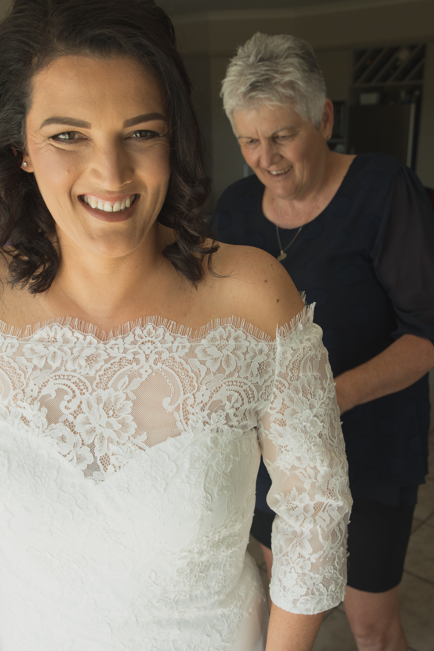 bride smiling and mother of the bride buttons up wedding dress