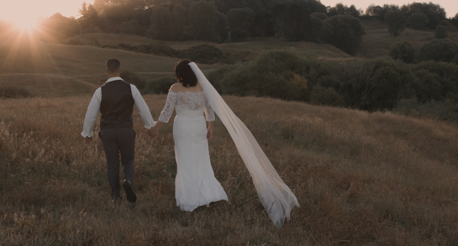 bride and groom walking into sunset on wedding day in long grass
