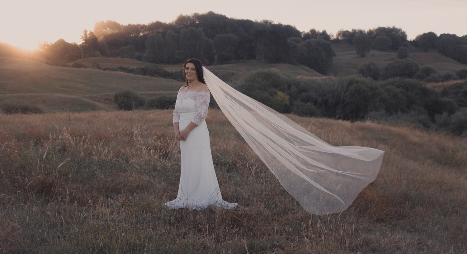 bride with veil floating at sunset on farm