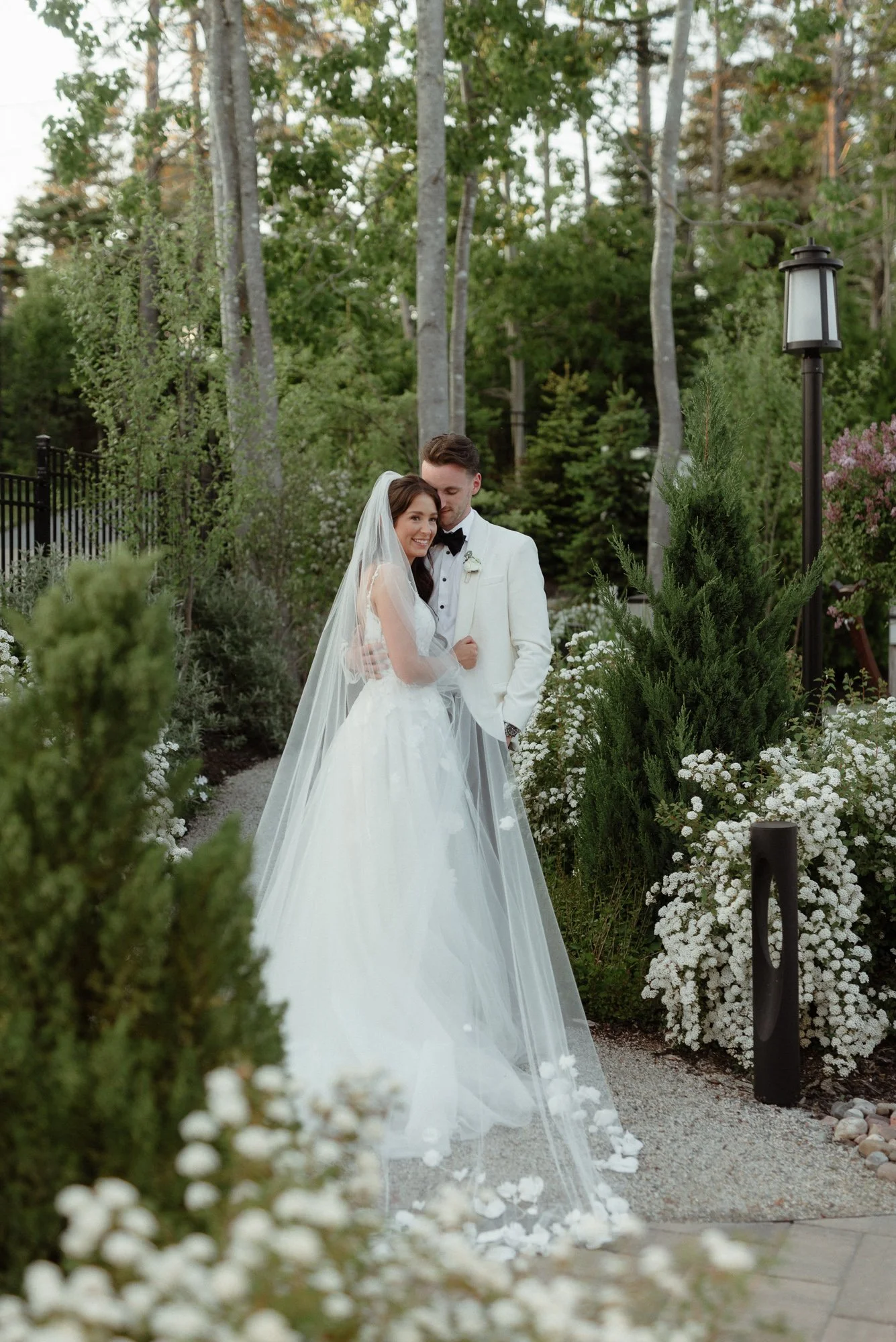 Bride and groom embracing in flower-lined garden path at Oceanstone Resort Nova Scotia