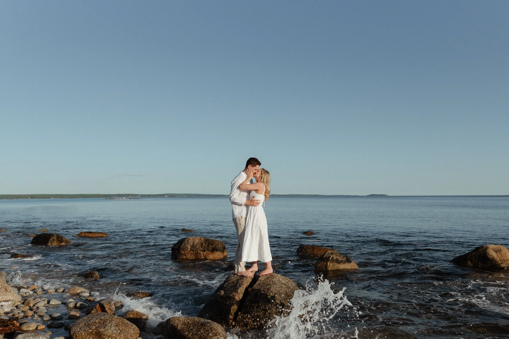 Engaged couple standing on rocky Nova Scotia south shore beach with ocean waves splashing