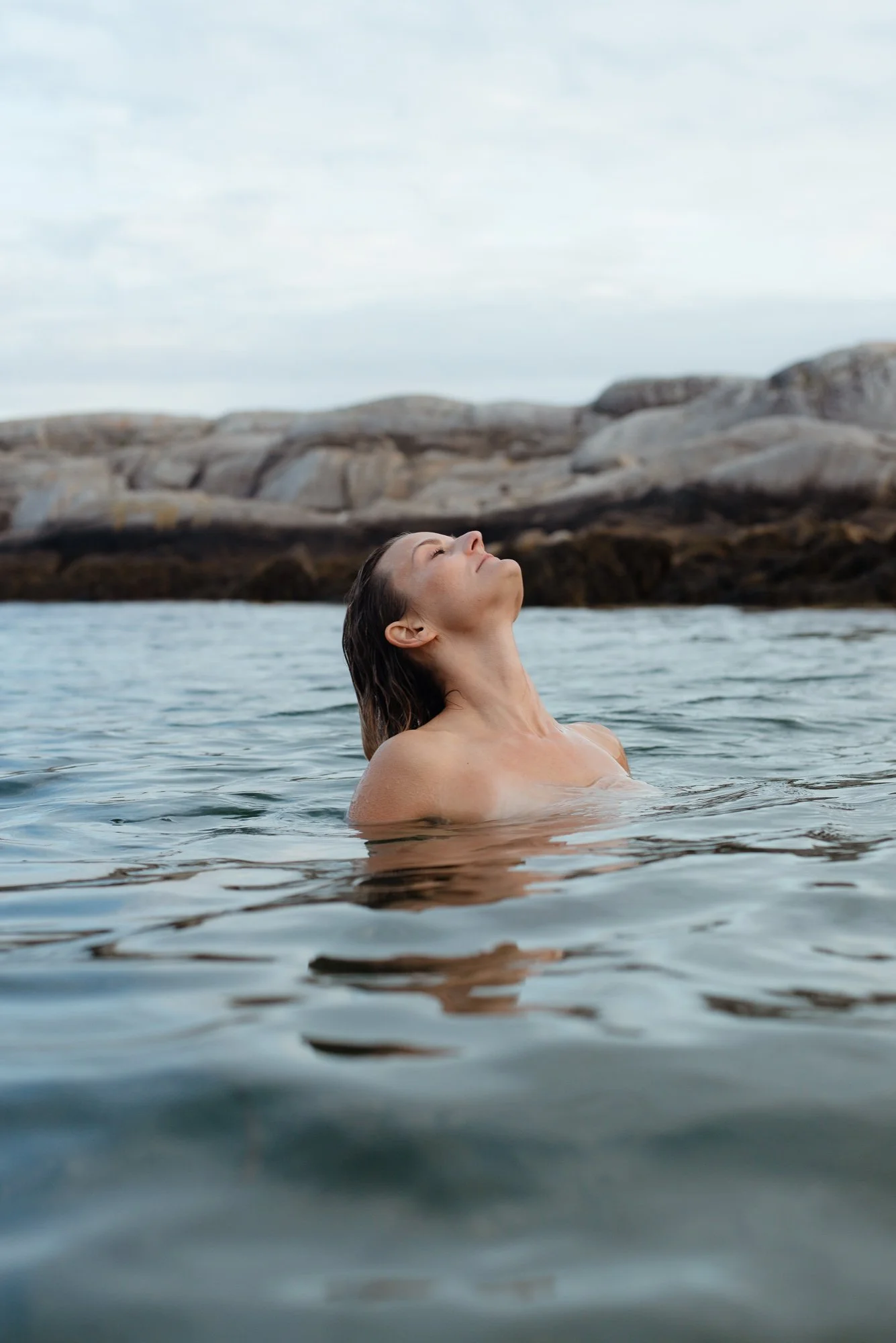 Woman swimming in ocean at Polly's Cove Nova Scotia with rocky coastline and soft light