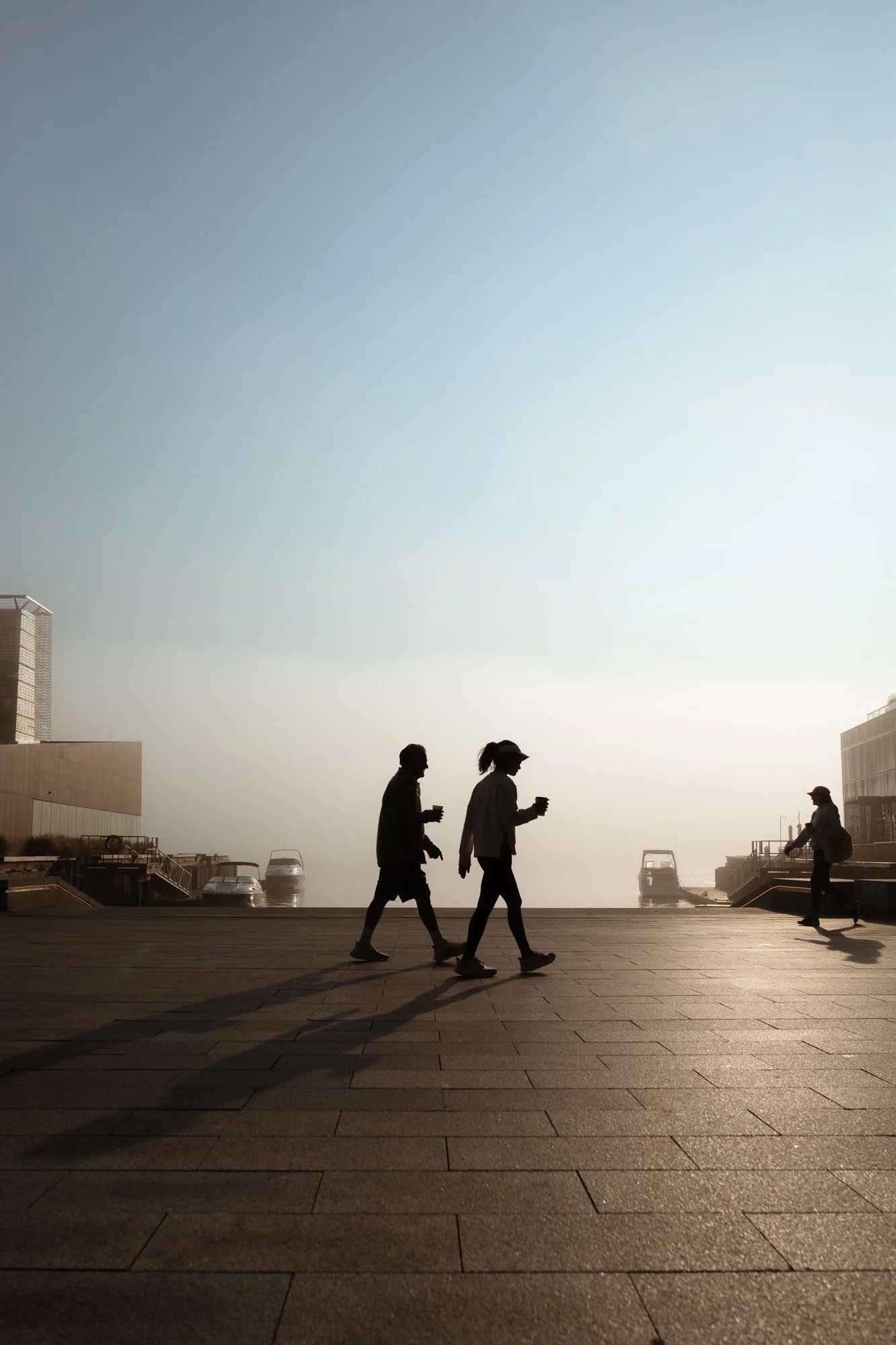 Two figures silhouetted walking past Tidal Beacon on Halifax waterfront's Queens Marque District at sunrise