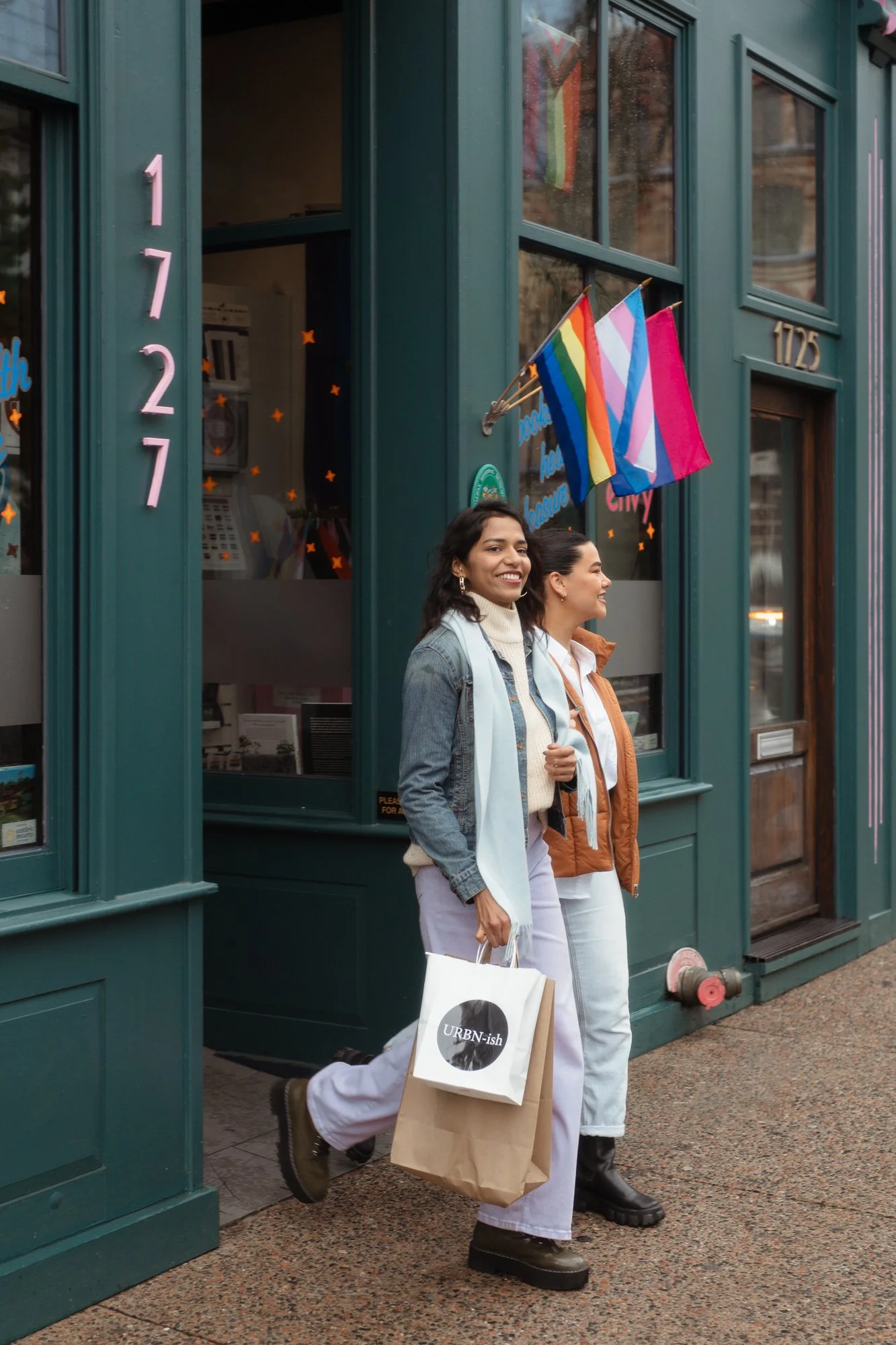 Two women laughing outside Venus Envy Halifax with pride and trans flags 