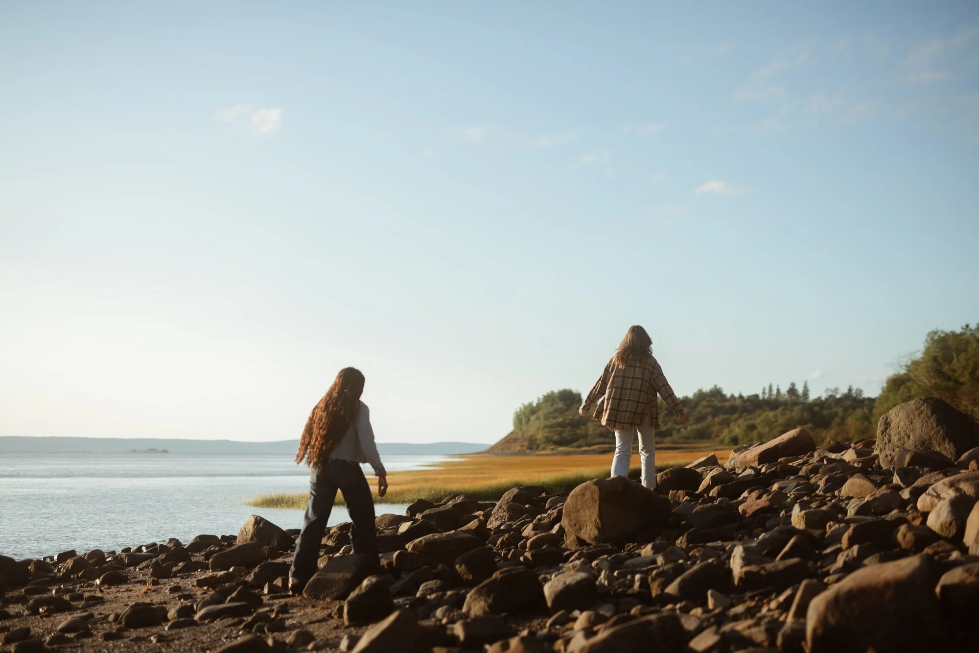 Two women walking together along rocky West Hants Nova Scotia coastline at sunset