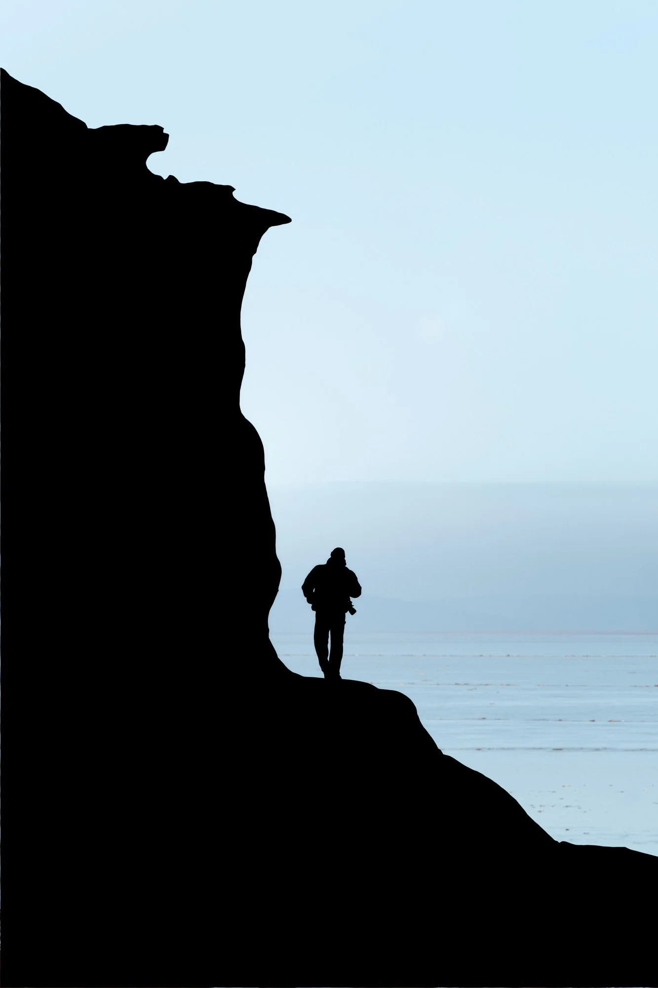 Lone figure silhouetted climbing rocky coastal cliff edge on the Bay of Fundy against calm ocean horizon
