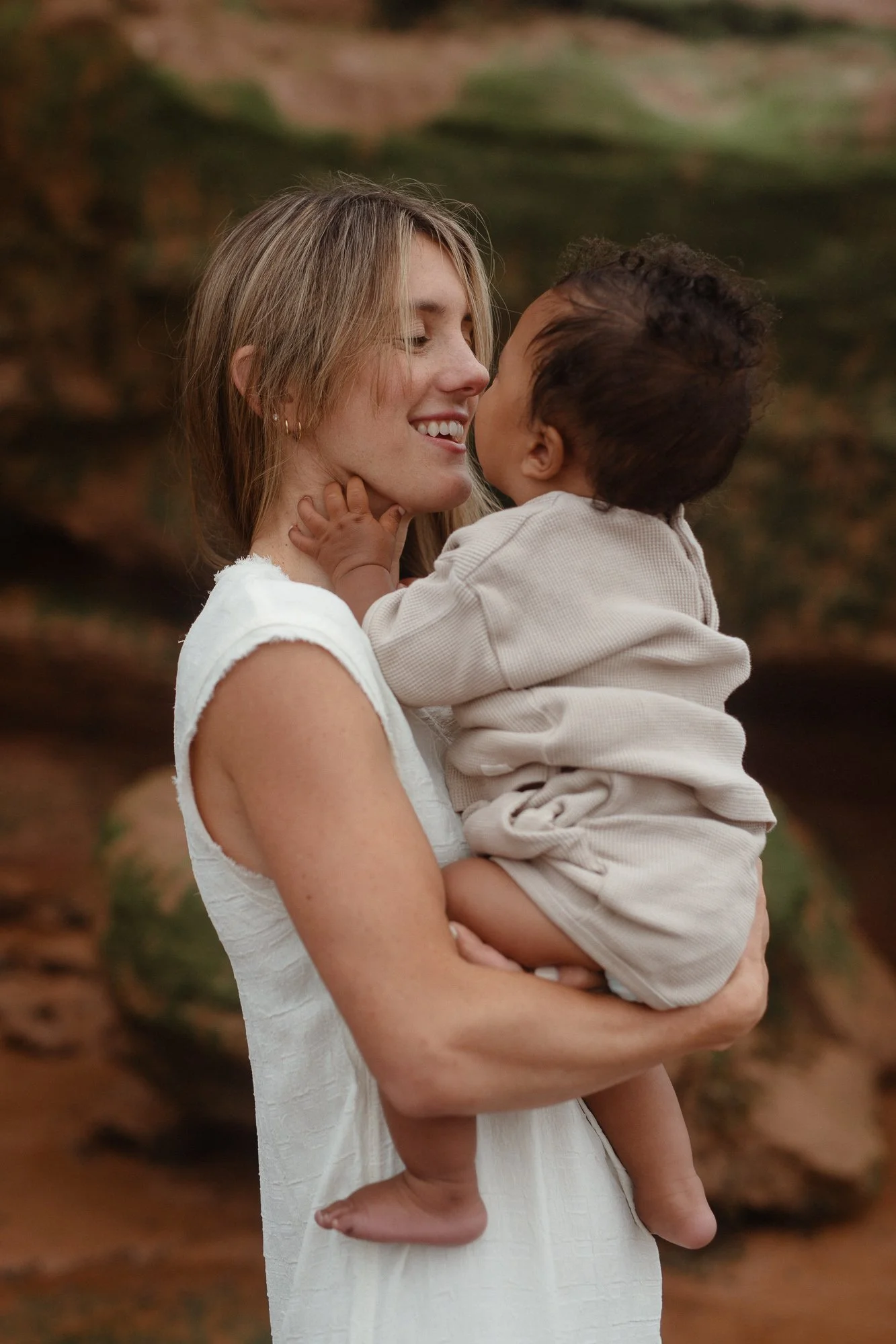 A woman holding a young child in a natural outdoor setting, smiling and touching noses.