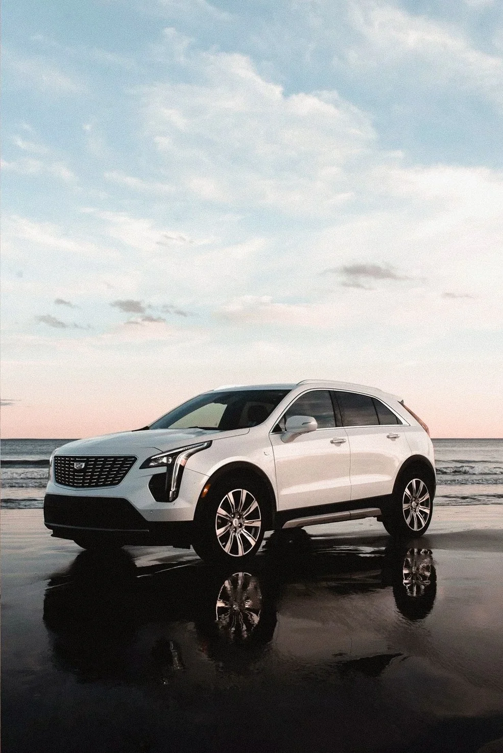 White Cadillac SUV on a reflective sandy beach at sunset, commercial photography