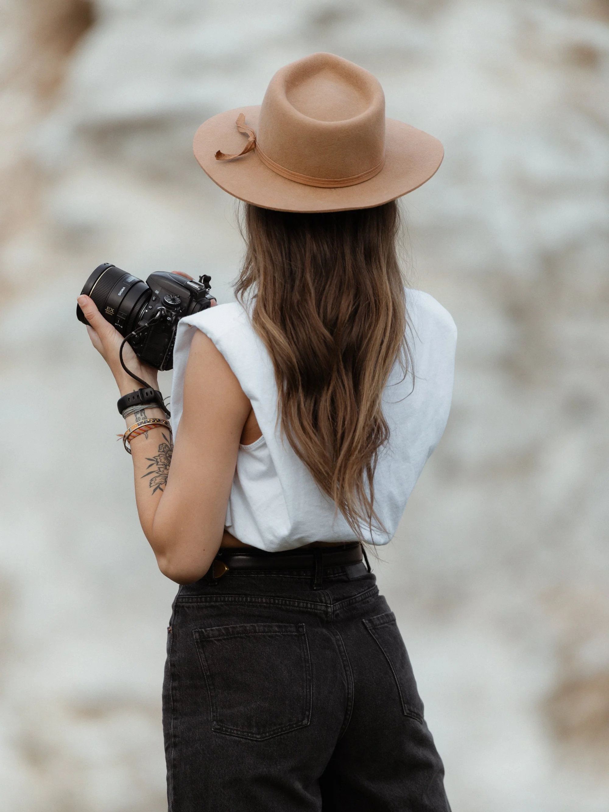 Halifax photographer Alexa Cude self-portrait from behind, holding her camera and wearing a wide brim hat