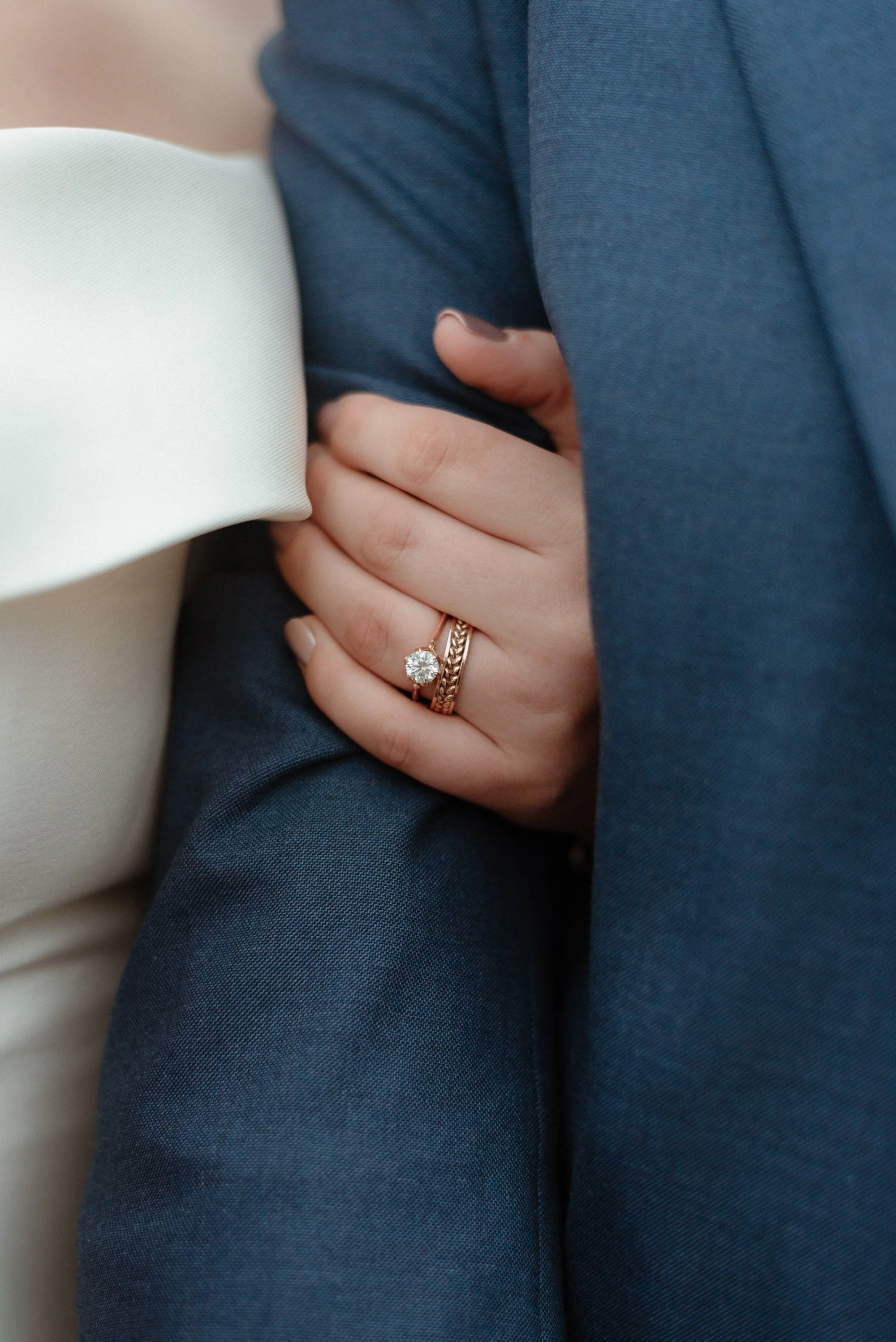 Close-up of an engagement ring and wedding band on a bride's hand resting on a groom's suit jacket