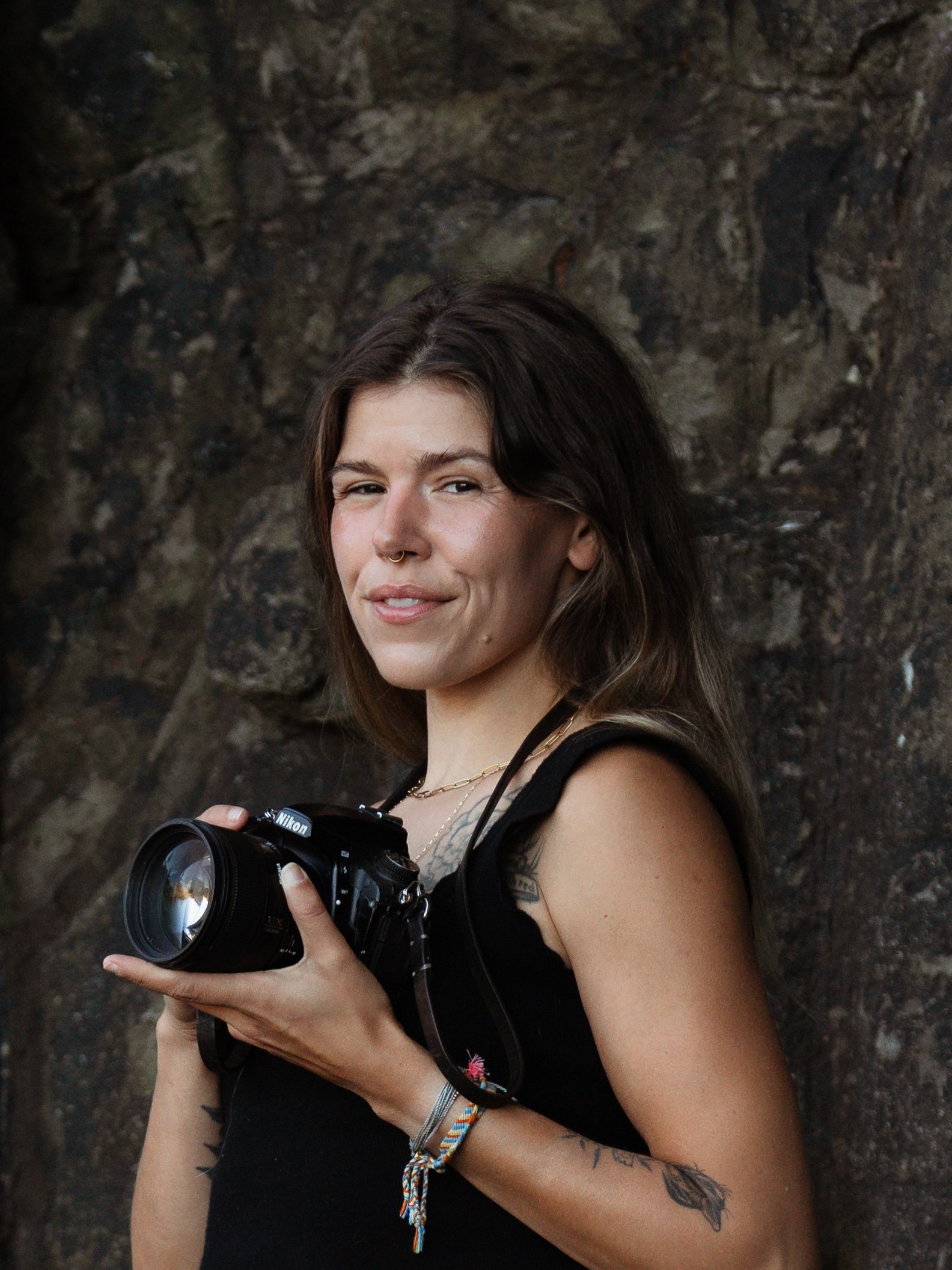Halifax wedding photographer Alexa Cude holding her Nikon camera up against a dark rock face