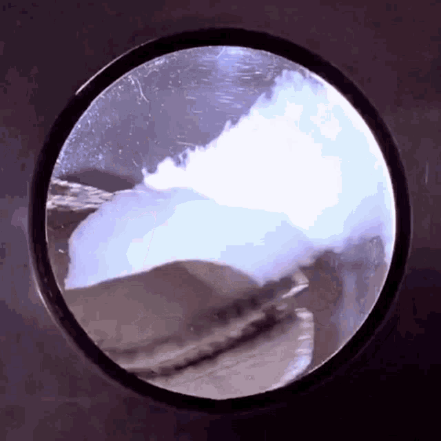 A GIF of Jurassic Park: a velociraptor peers through a circular window, then breathes on it. The breath steams up the window ominously.