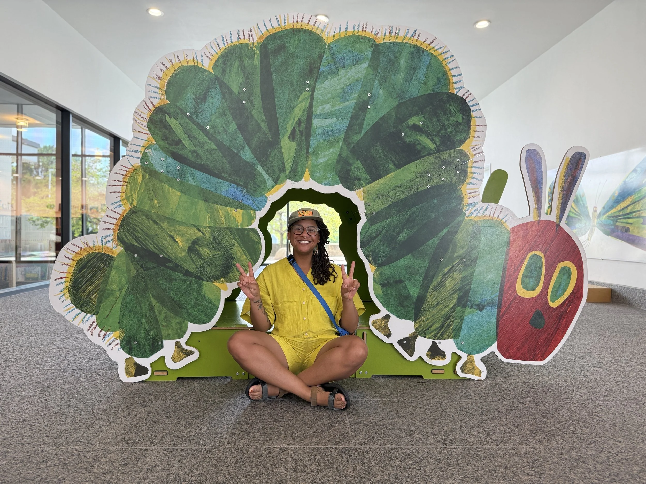 Jewel Davis sitting inside a large caterpillar sculpture at the Eric Carle Museum of Picture Book Art.