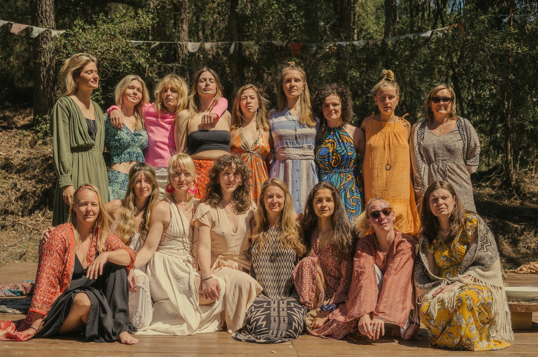 Group of women posing outdoors on a wooden platform, surrounded by trees and greenery.
