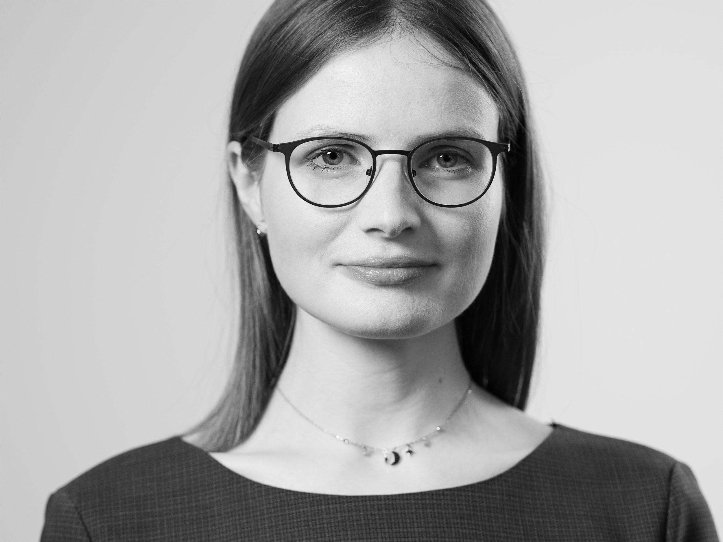 Schwarz-weiß Porträt einer Frau mit Brille und langen Haaren, sie trägt eine Kette und ein kariertes Oberteil.