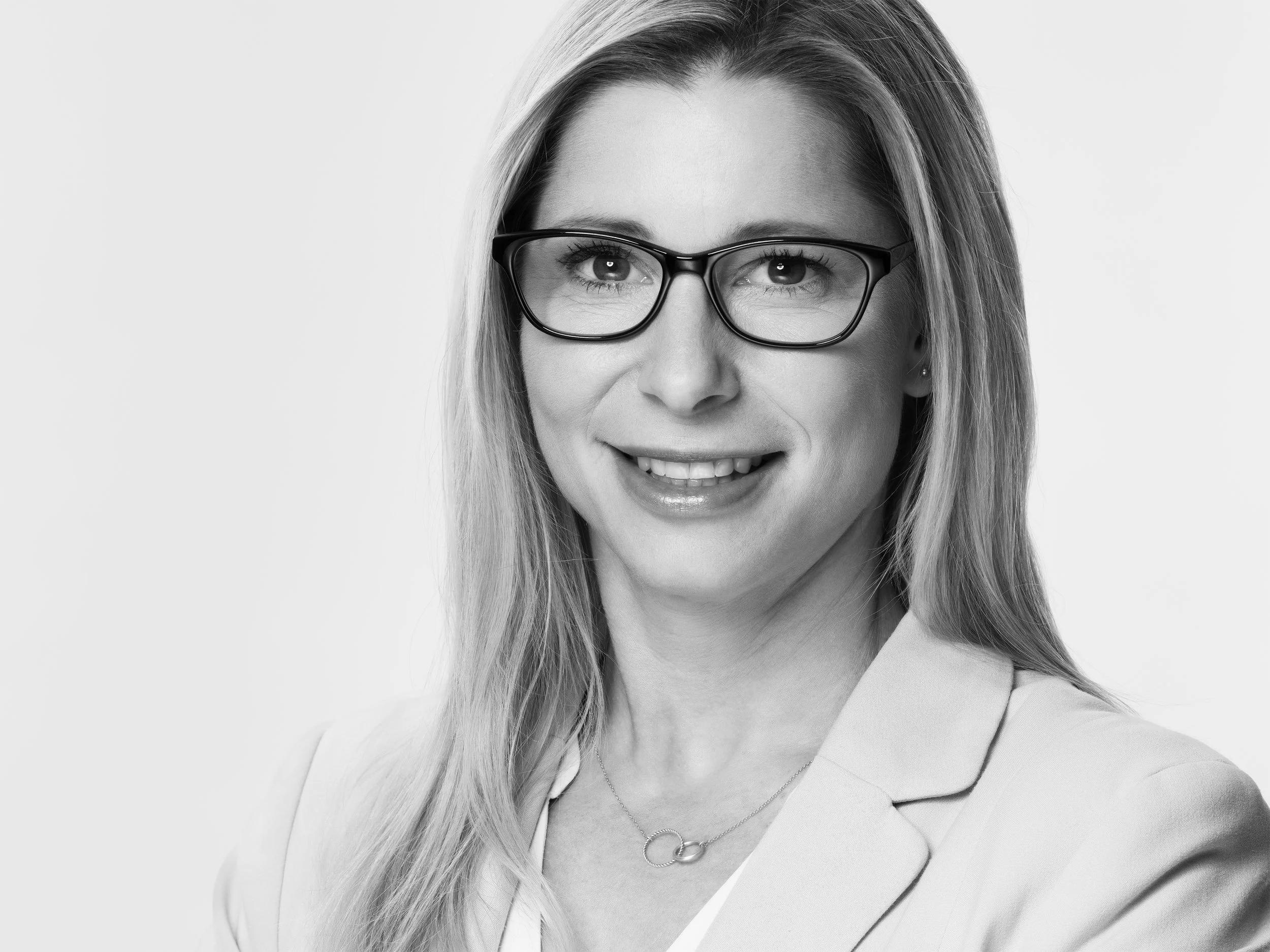 Schwarz-Weiß-Foto einer lächelnden Frau mit Brille und langen, glatten Haaren.