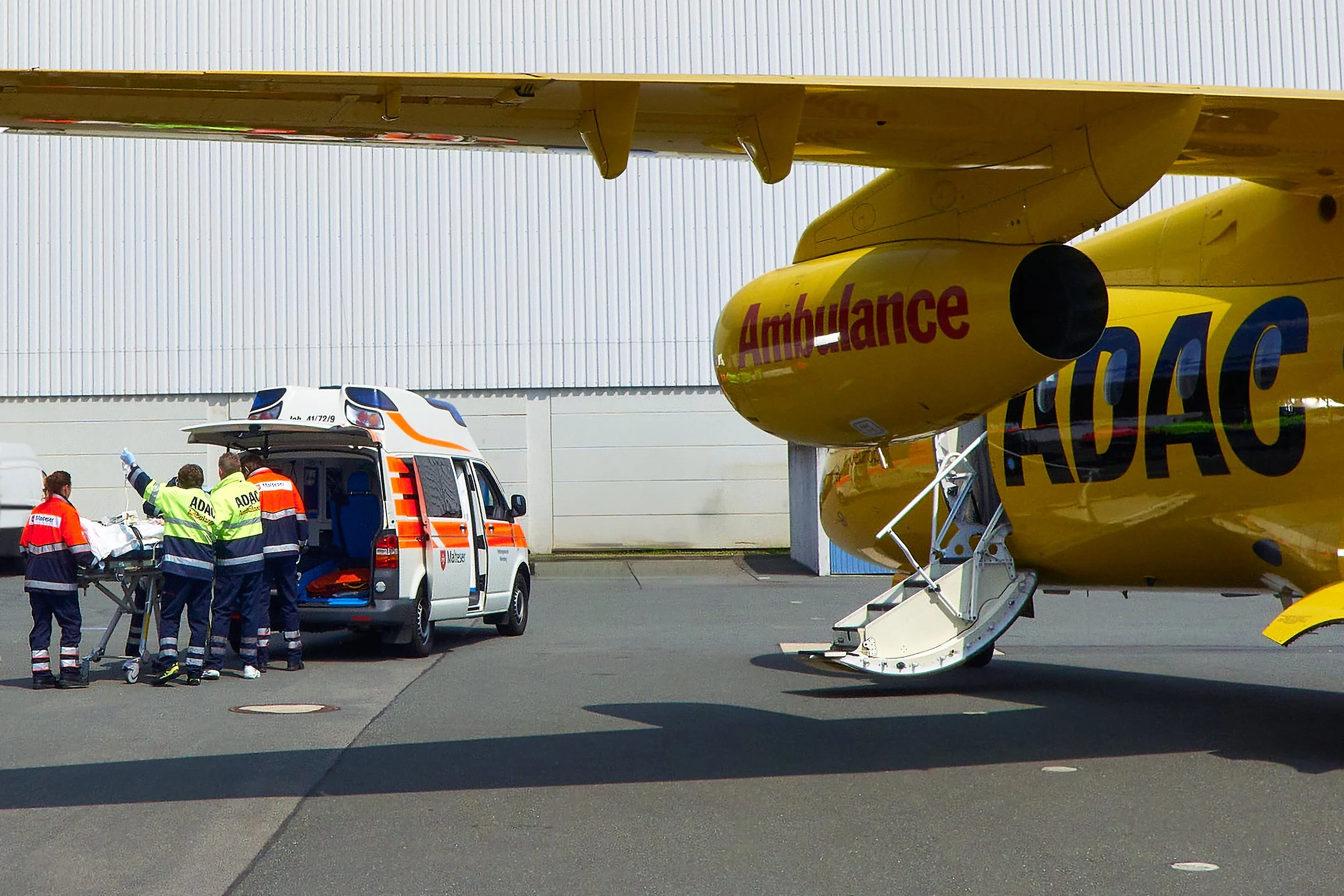 Rettungsdienstpersonal beim Einsatz neben einem gelben Rettungsflugzeug vom Typ Air Ambulance, das am Boden steht, bei einem Flughafen.